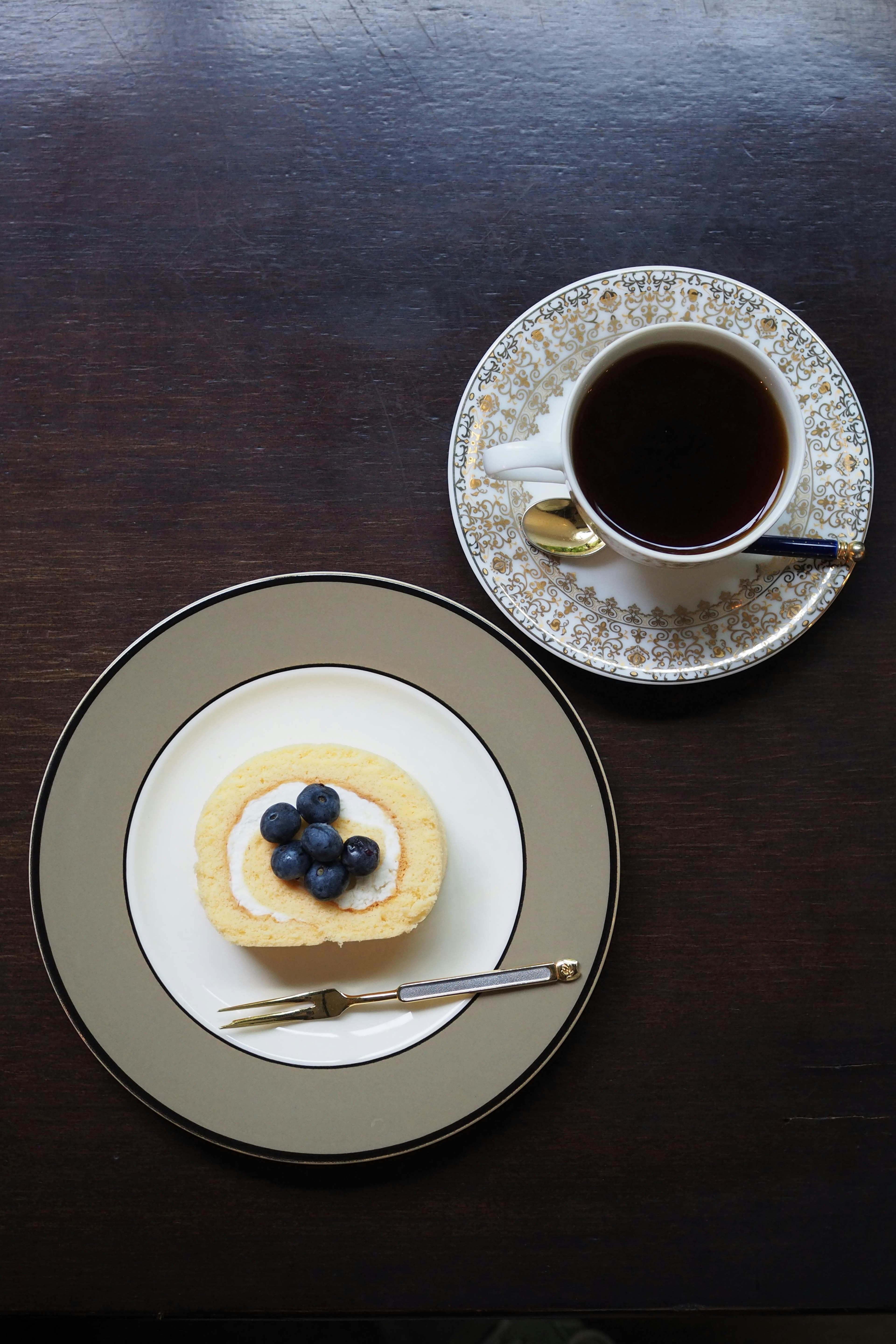 Piring dengan makanan penutup blueberry dan secangkir kopi di atas meja kayu