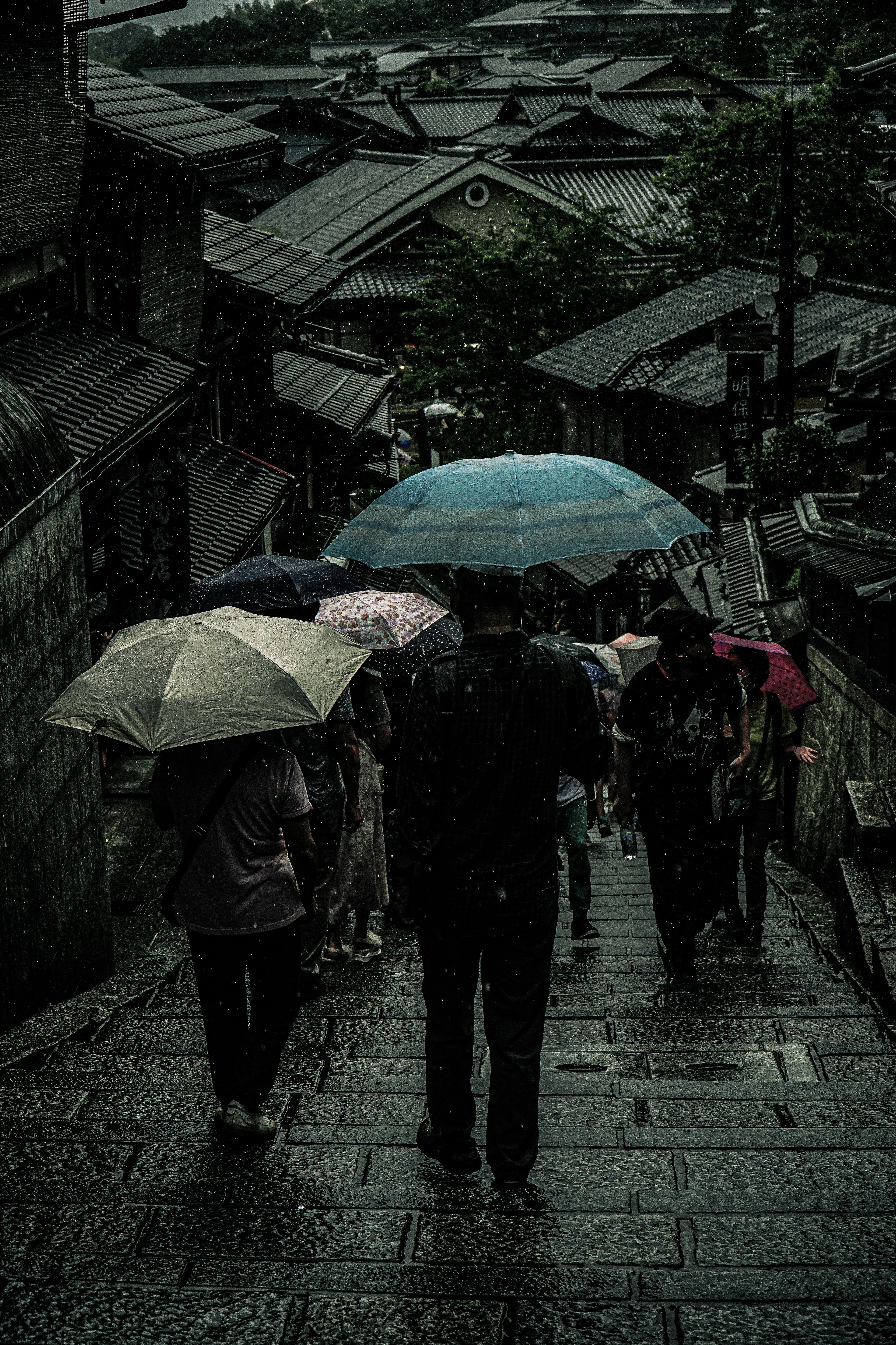 雨の中を歩く傘を持った人々と石の階段の景色