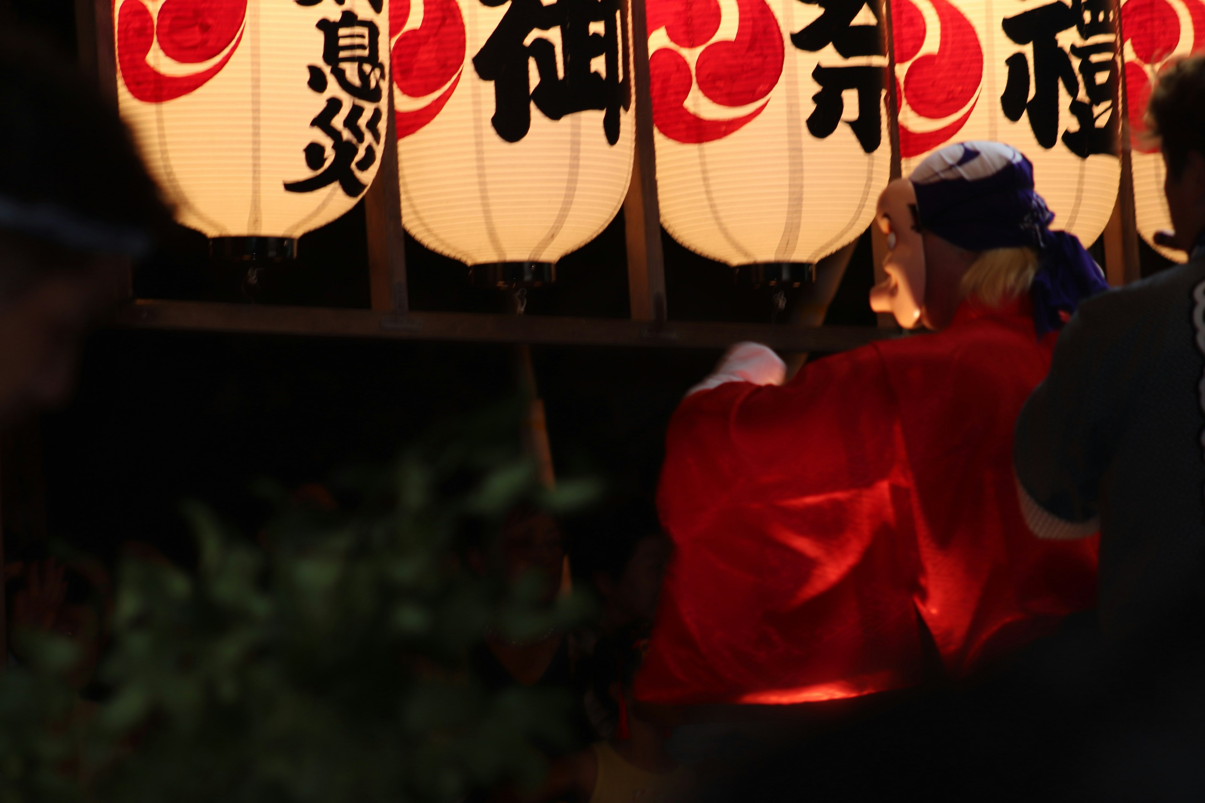 夜の祭りで提灯の前に立つ人物赤い衣装と白い提灯