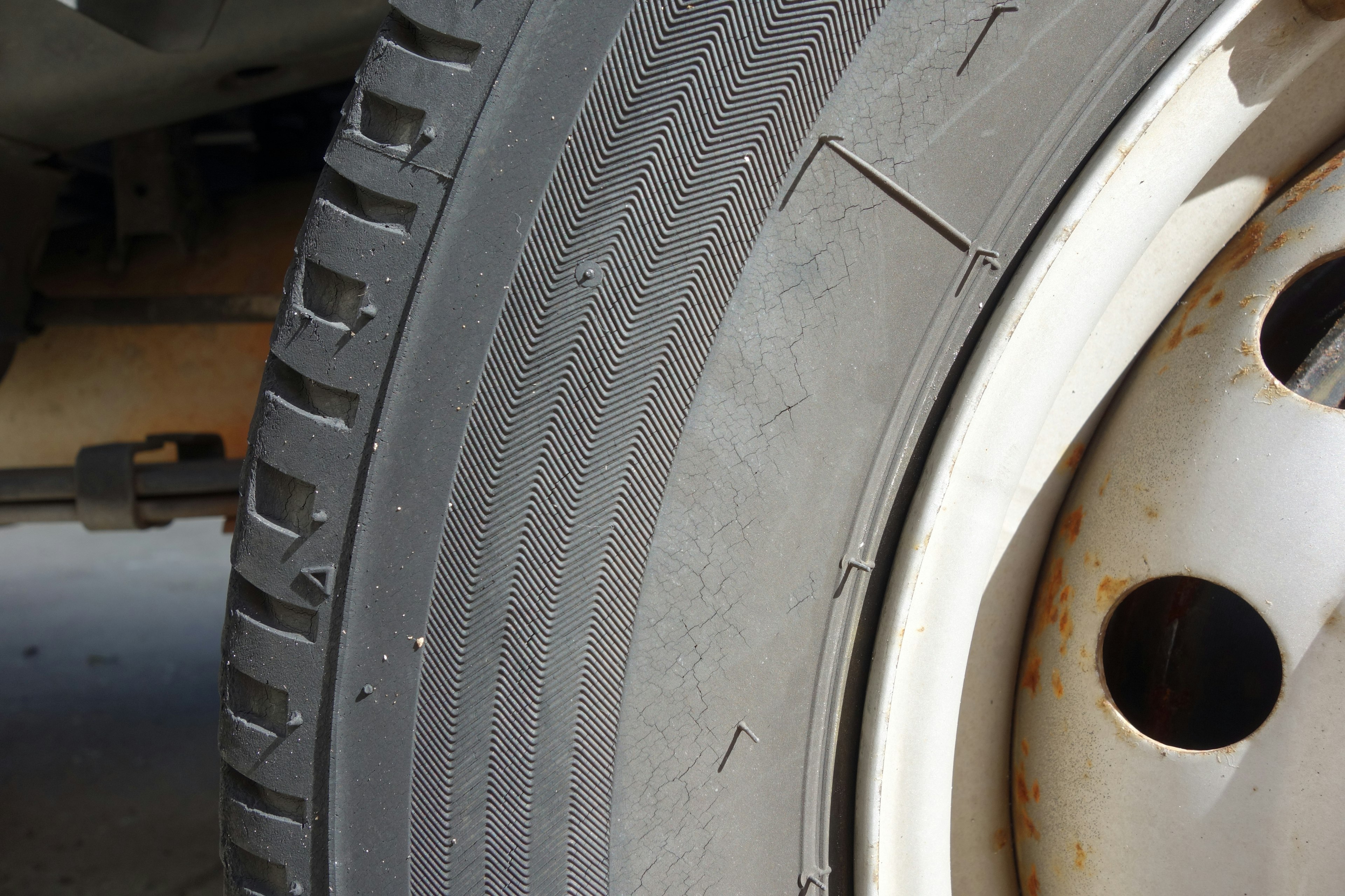 Close-up of a car tire showing worn tread and a white wheel