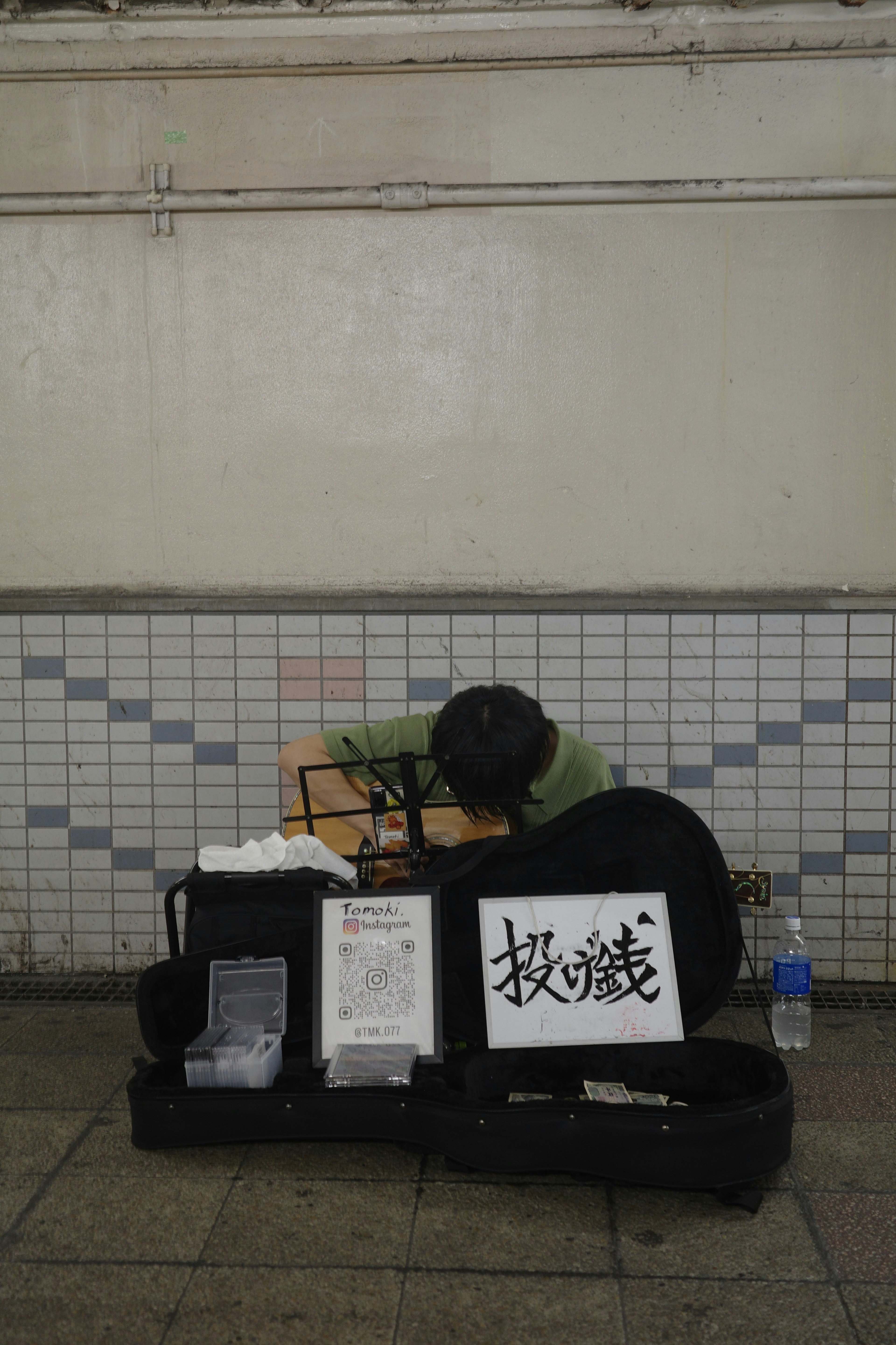 A person playing an instrument in an underground passage with an instrument case