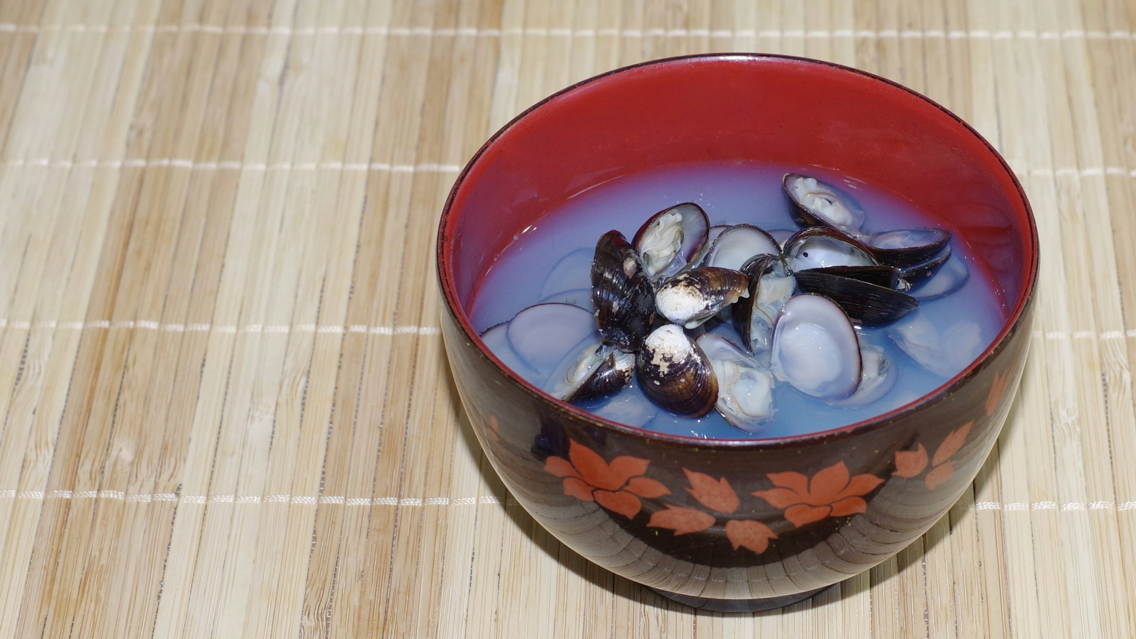 A red bowl containing shellfish soup on a wooden table