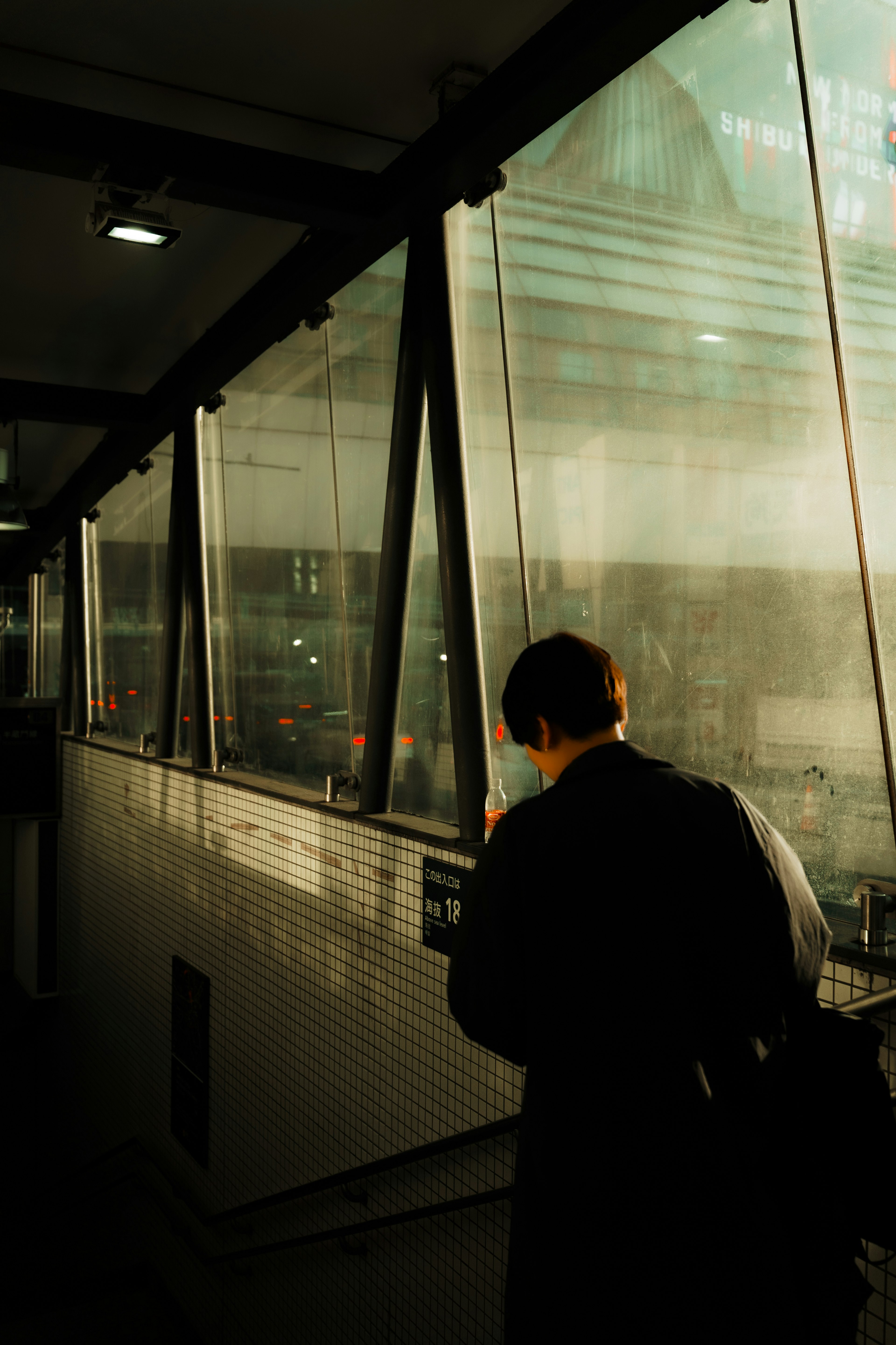 A person walking in a glass corridor dim lighting with reflections of the outside