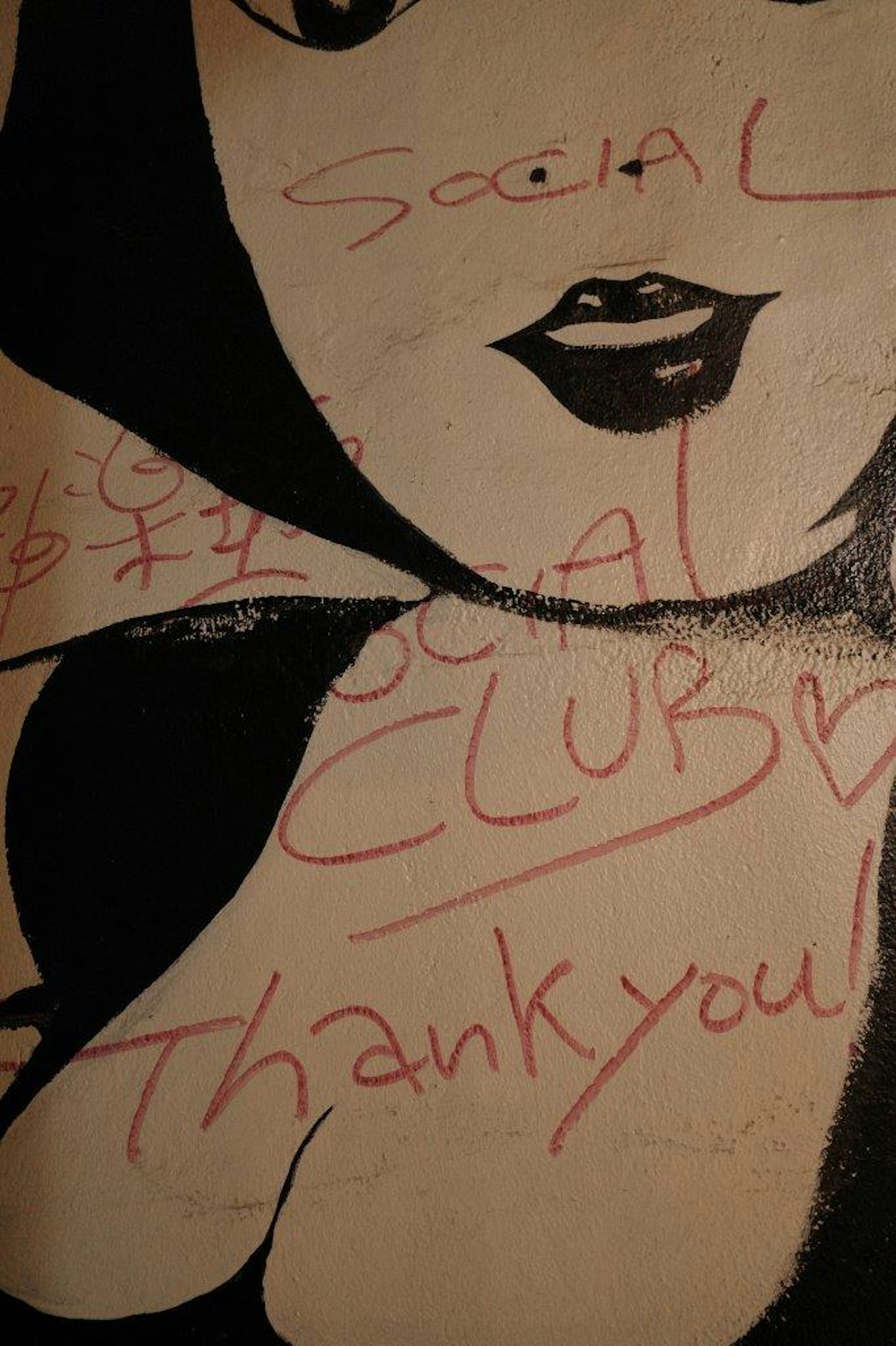 Grafiti de un rostro femenino en una pared con texto rojo que dice Club Social y Gracias