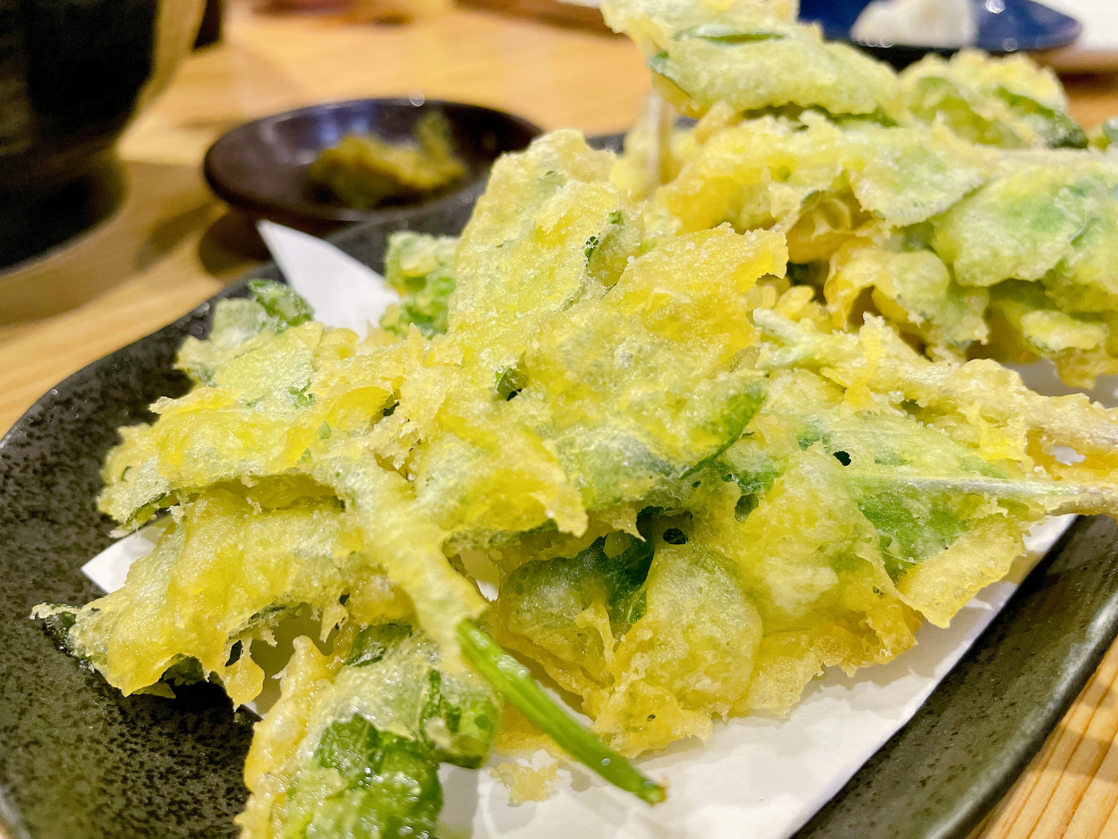 Ein Teller mit gemischtem Tempura mit knusprigem gelbem Teig und grünen Gemüse