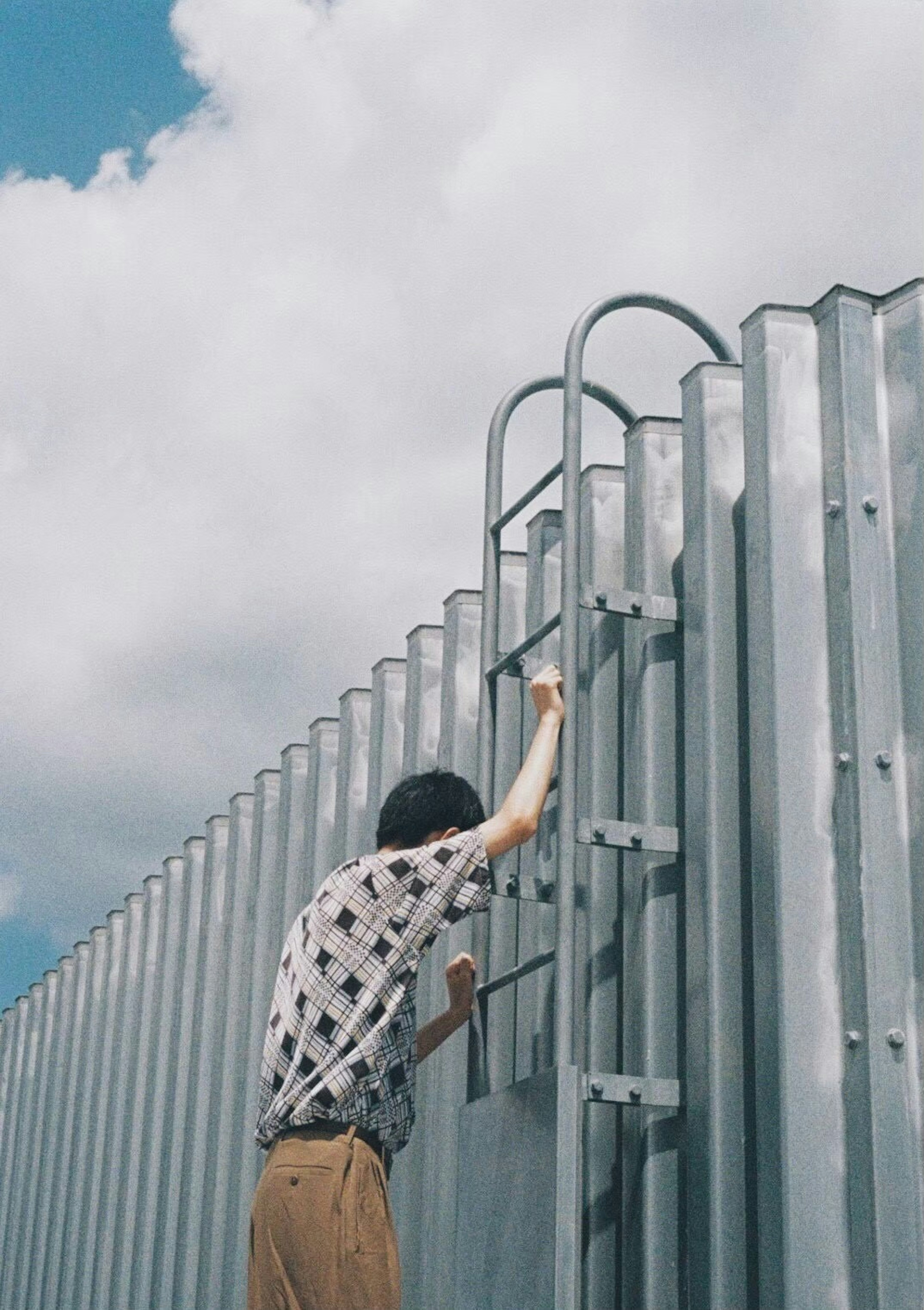 A person climbing a metal ladder against a blue sky