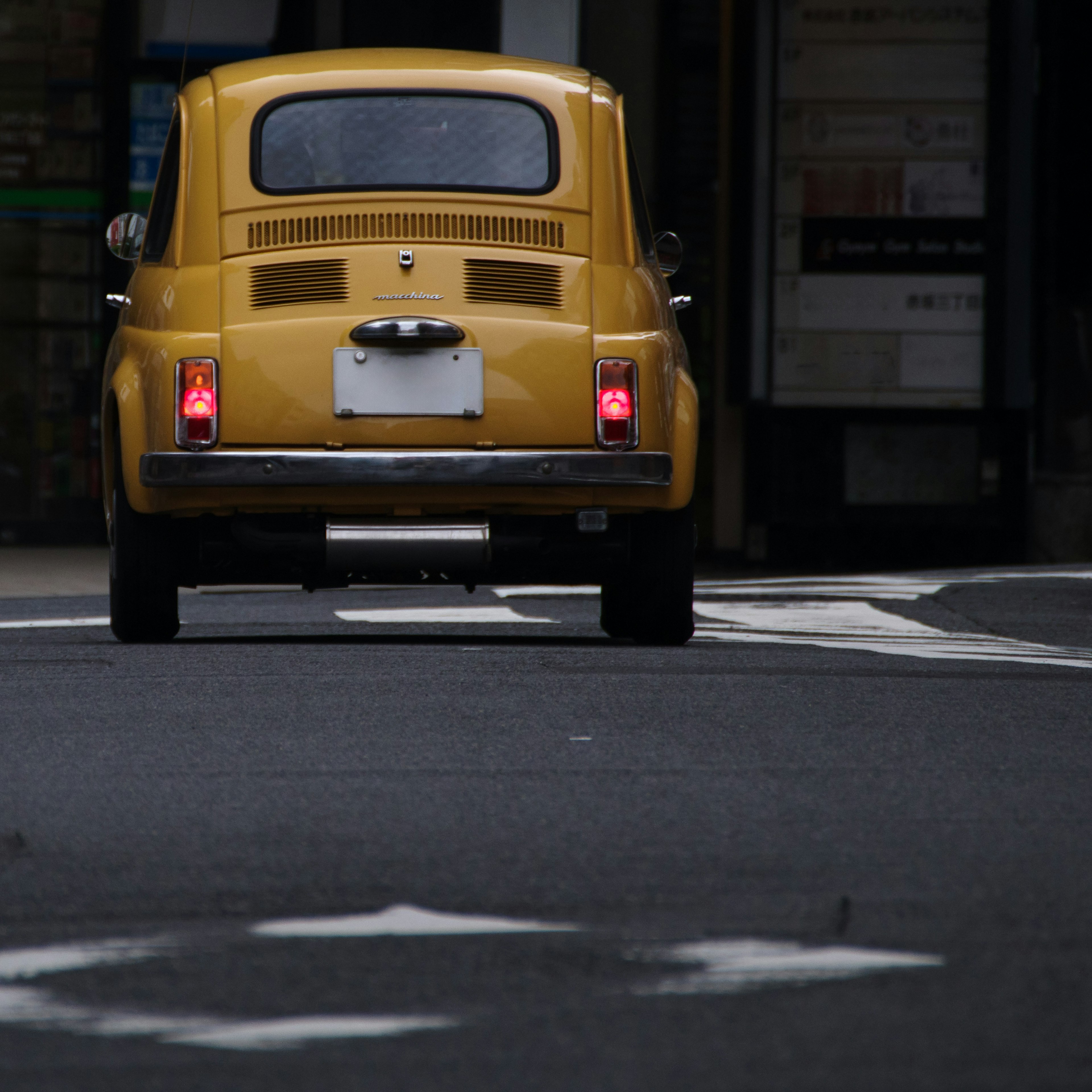 Yellow classic car driving down the street from behind