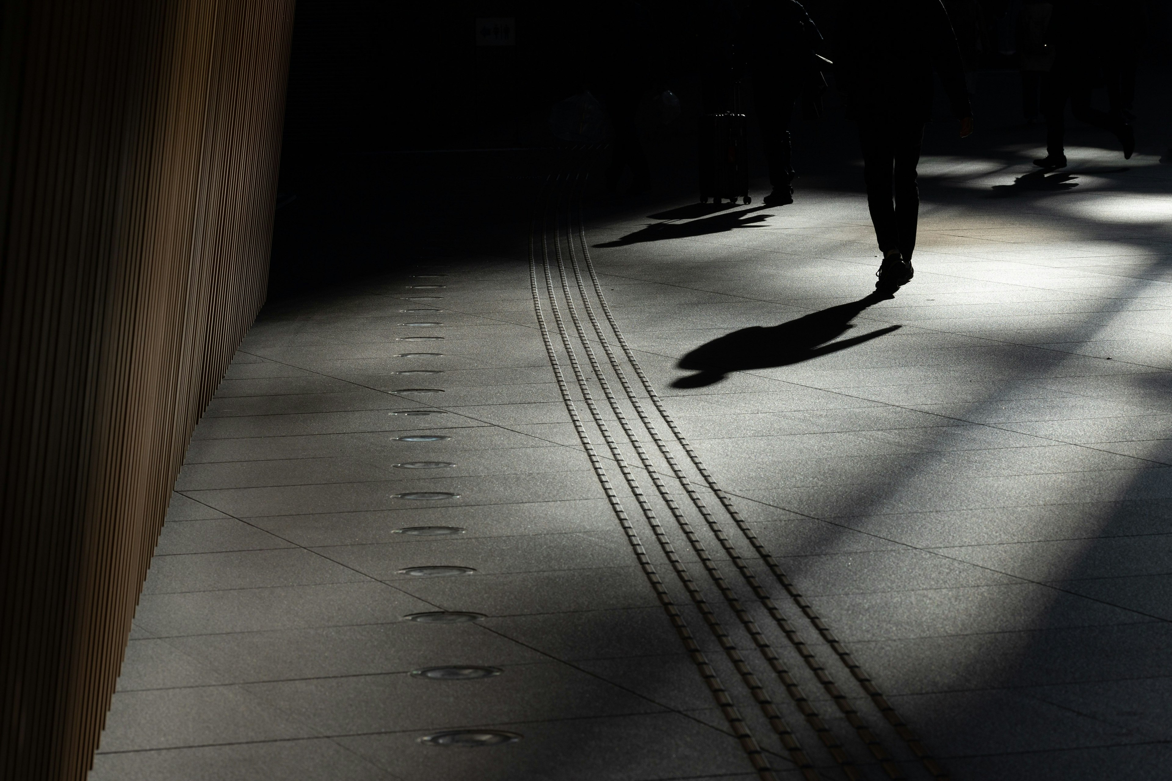 Silhouette di una persona che cammina nell'ombra con linee sul pavimento in un contesto urbano