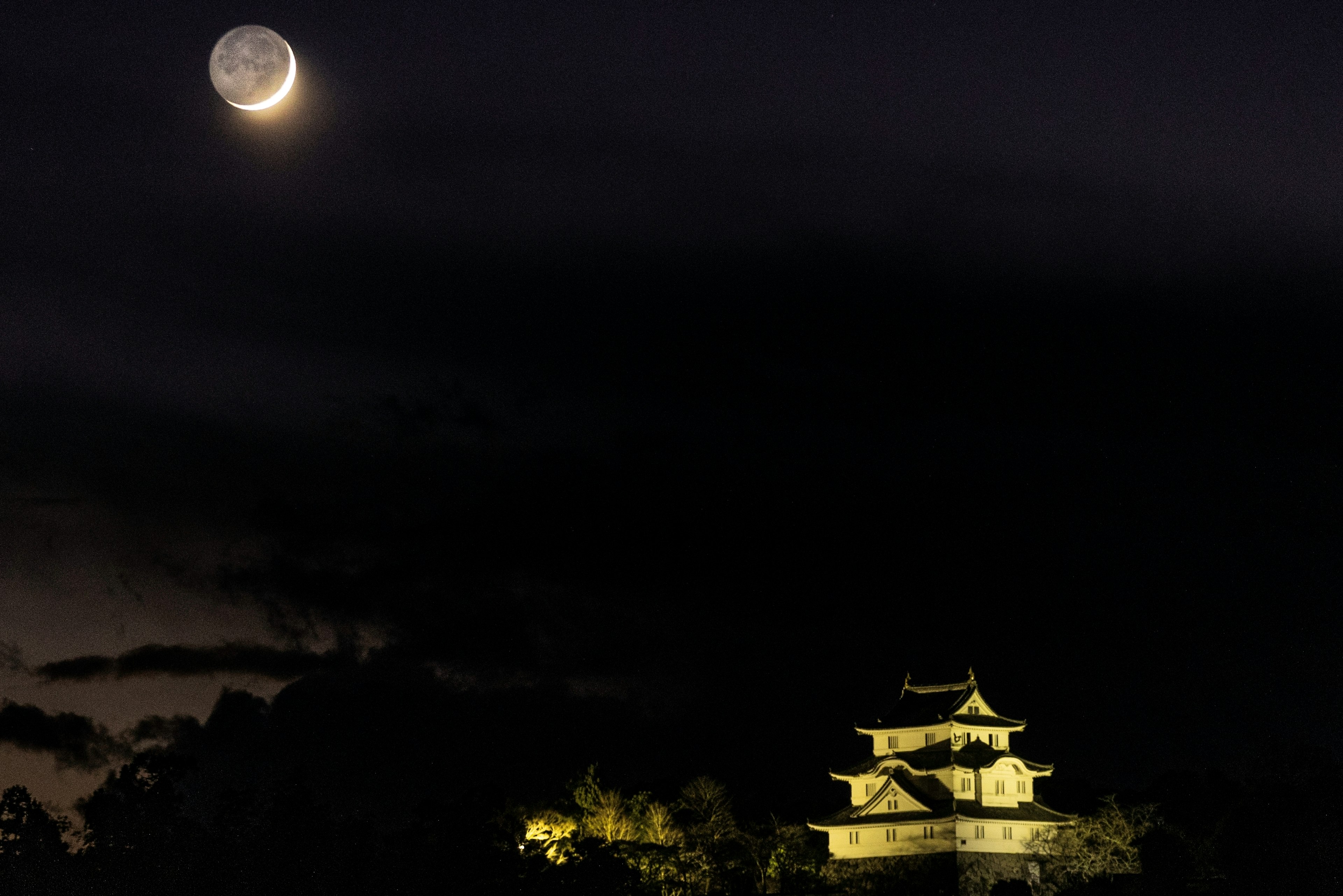 A crescent moon illuminating a castle at night with dark clouds