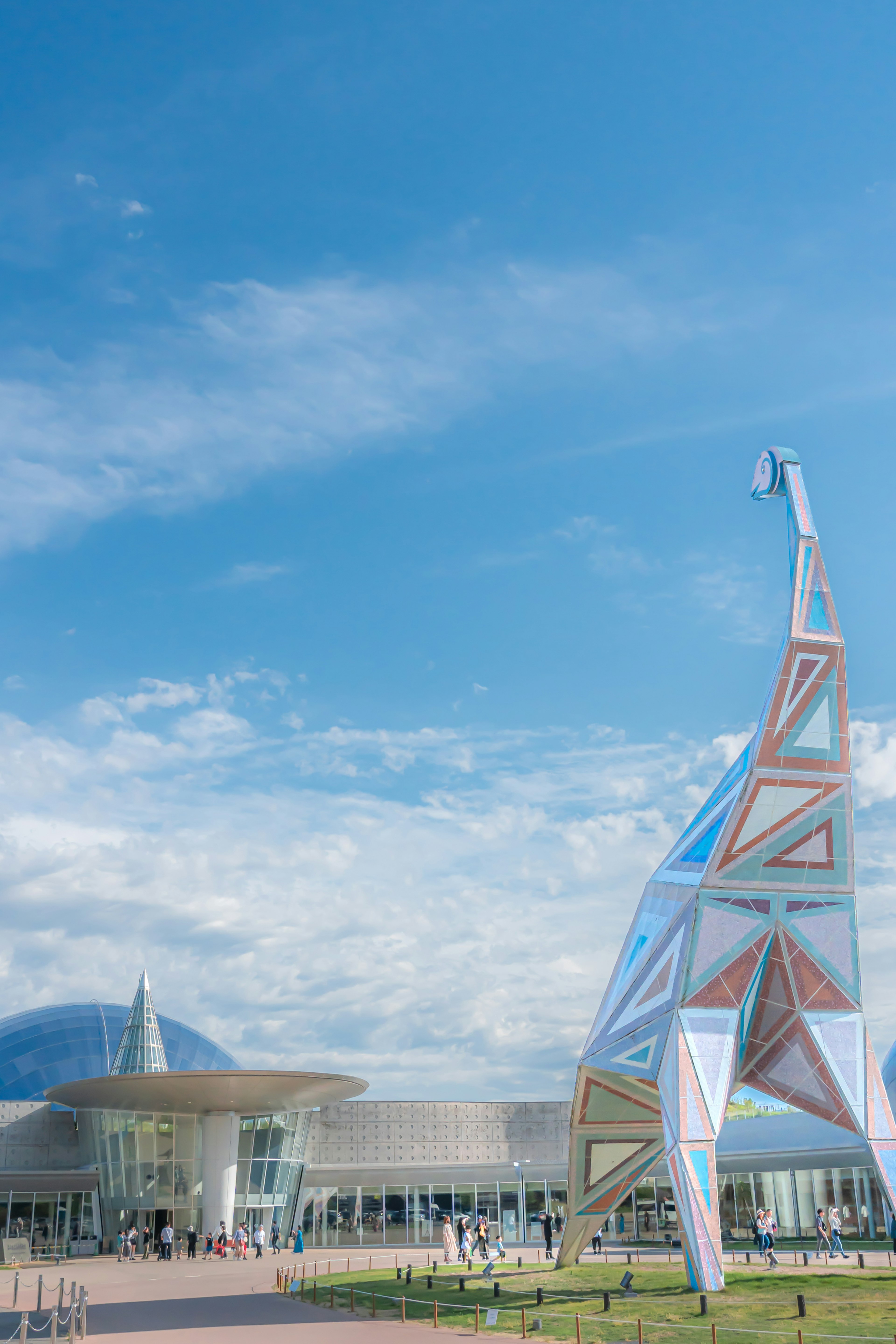 Colorful giraffe sculpture under blue sky with modern building