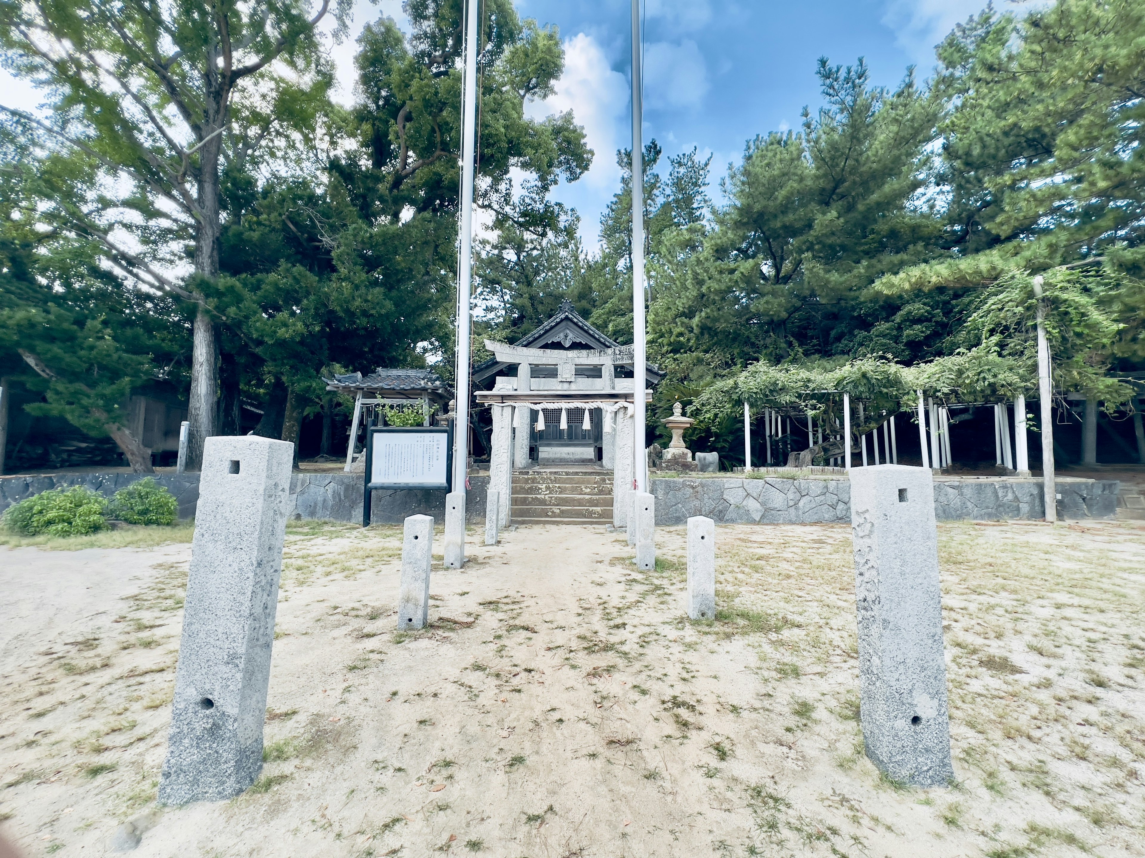 神社の入口と周囲の木々と石の柱が見える風景