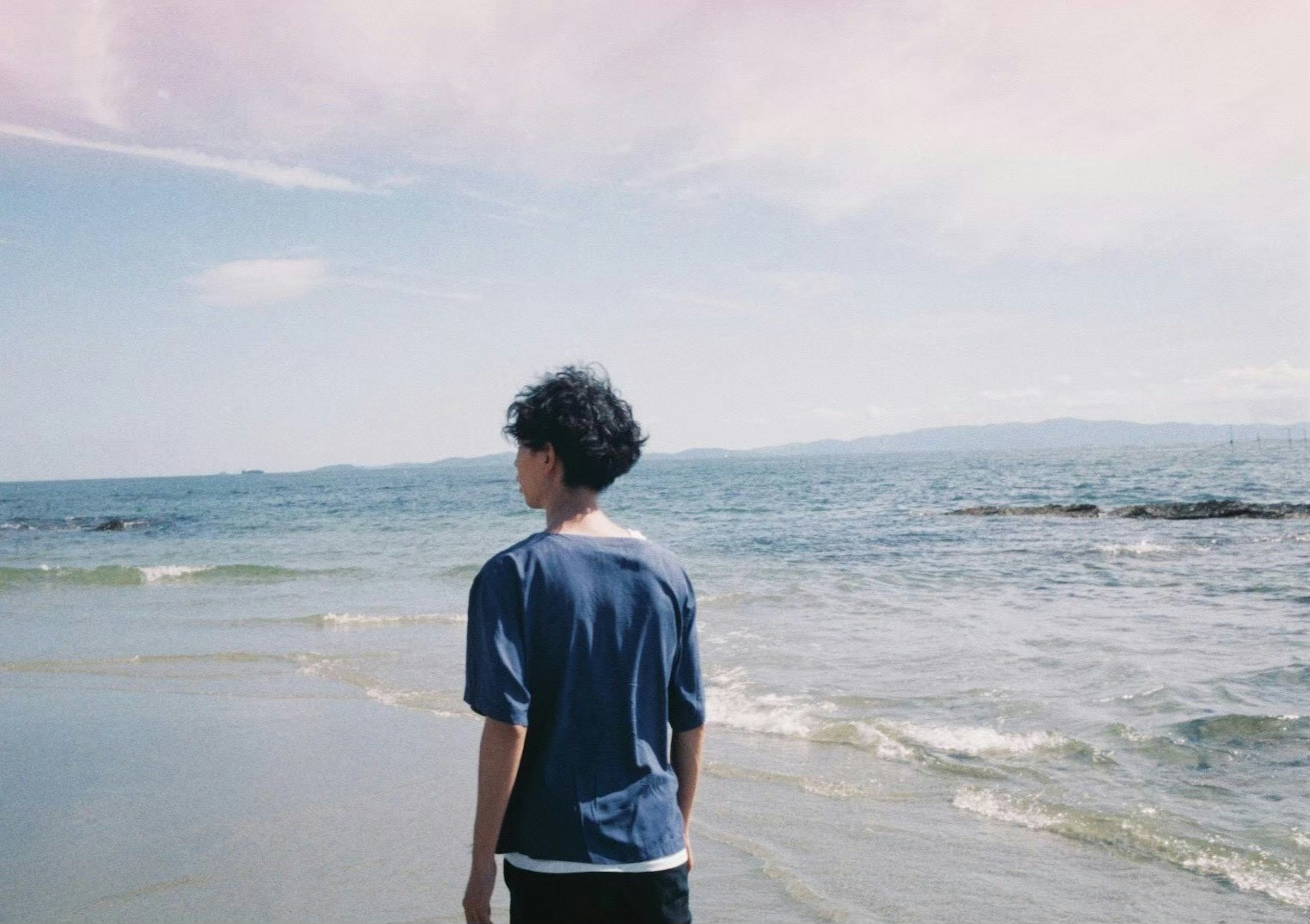 Silhouette of a young person facing the ocean at the beach with a blue sky