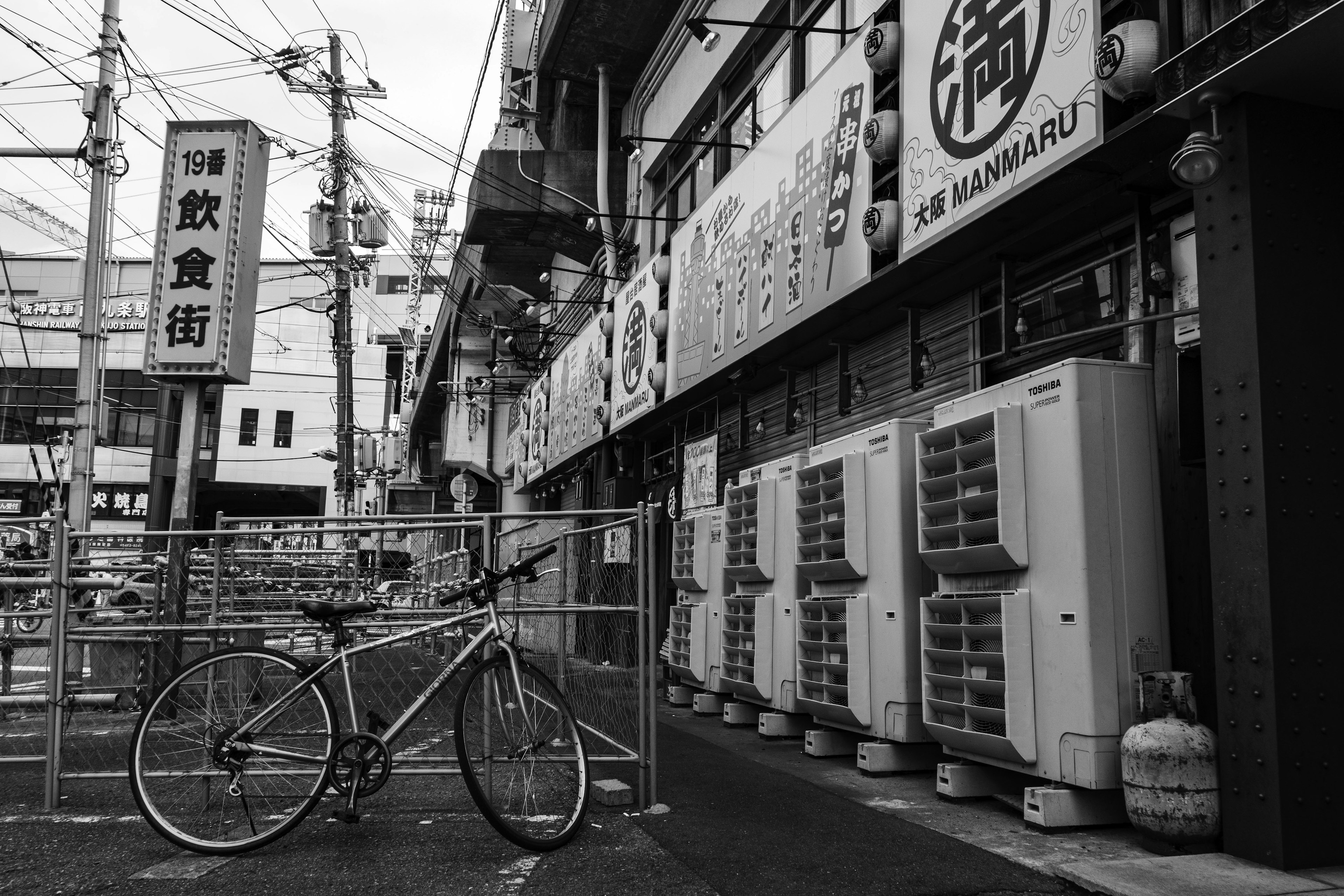 Black and white street scene featuring a parked bicycle and restaurant signs