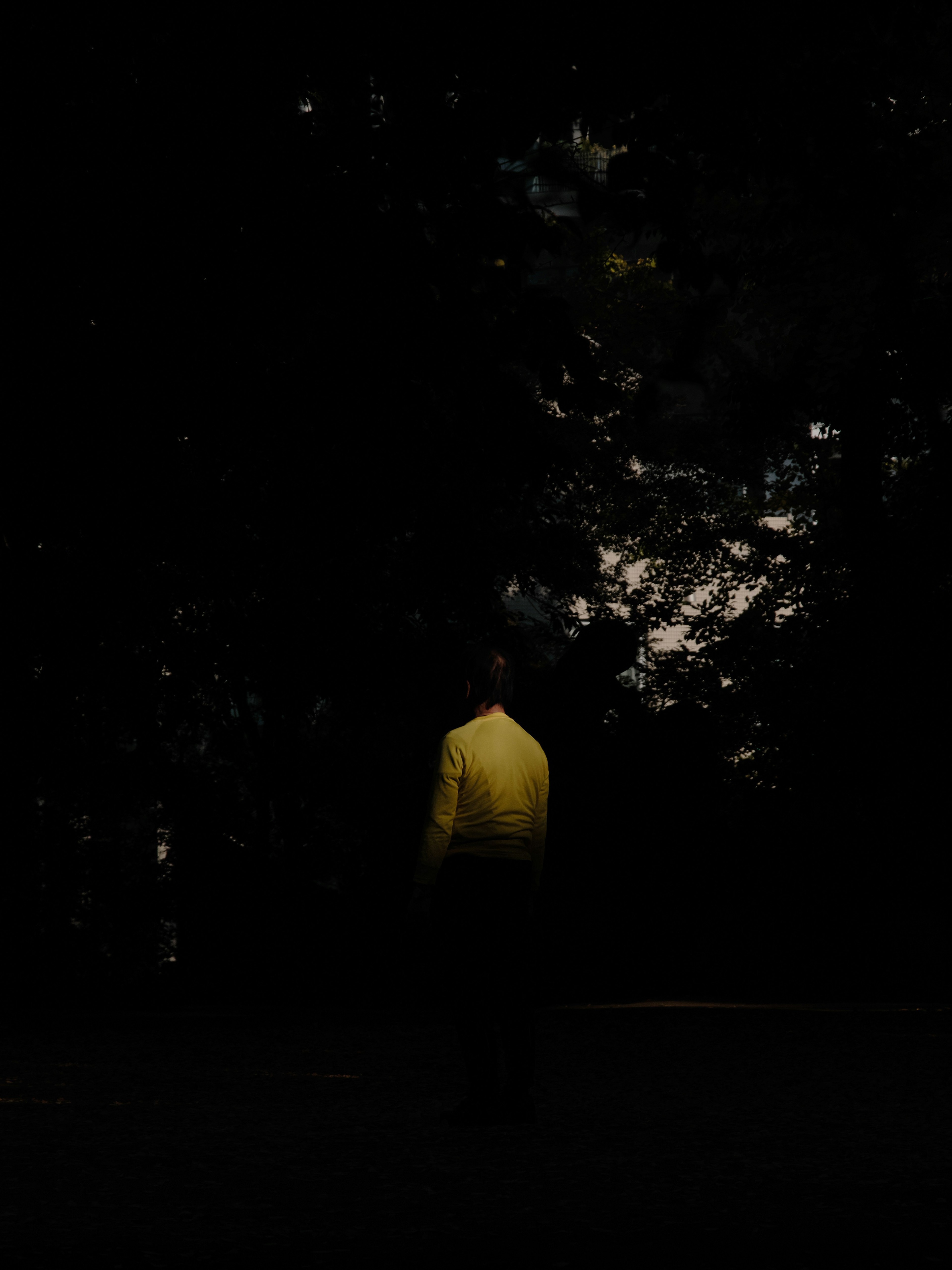 A figure in a yellow shirt standing against a dark background