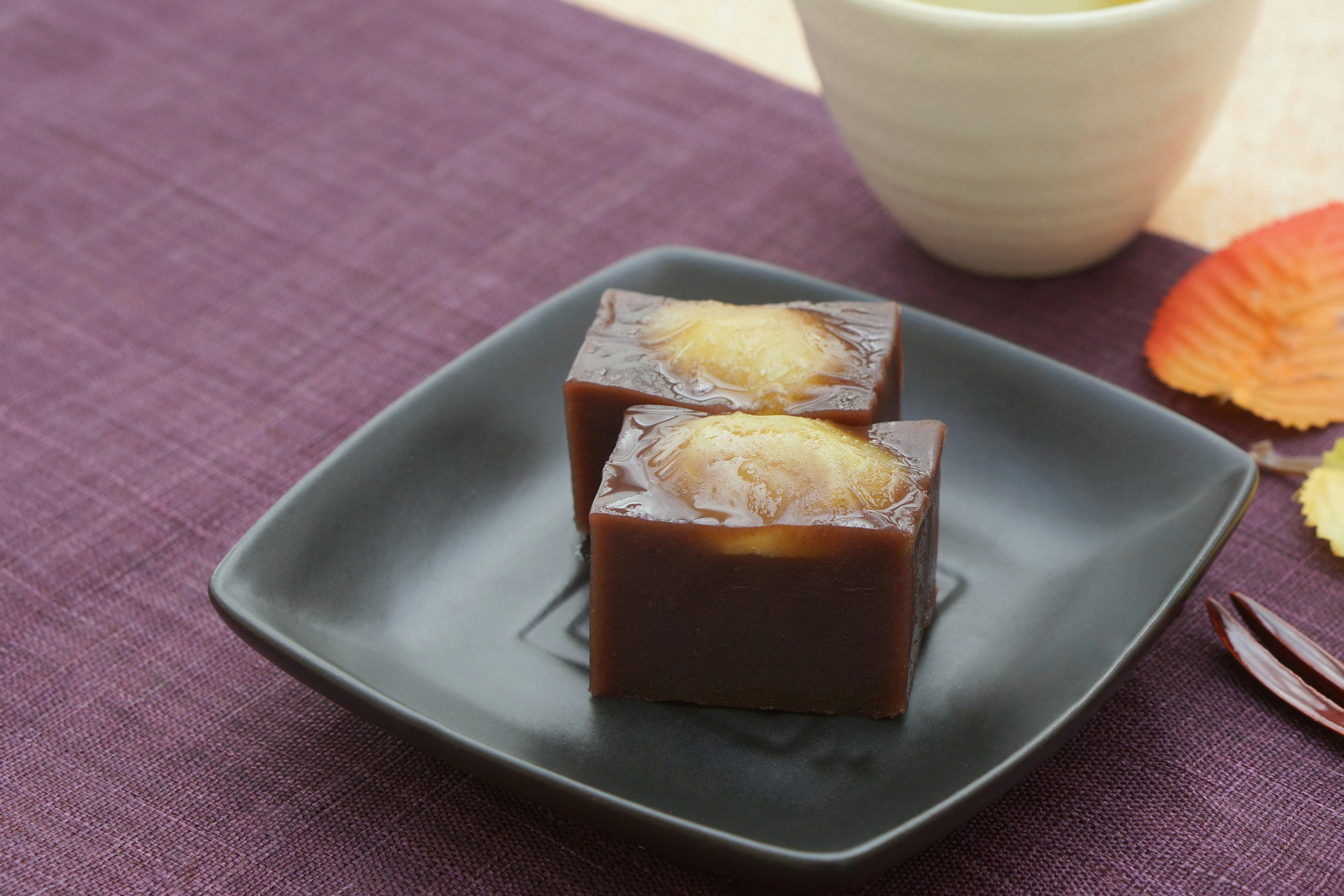 Japanese sweets on a black plate with a cup of tea on a purple tablecloth