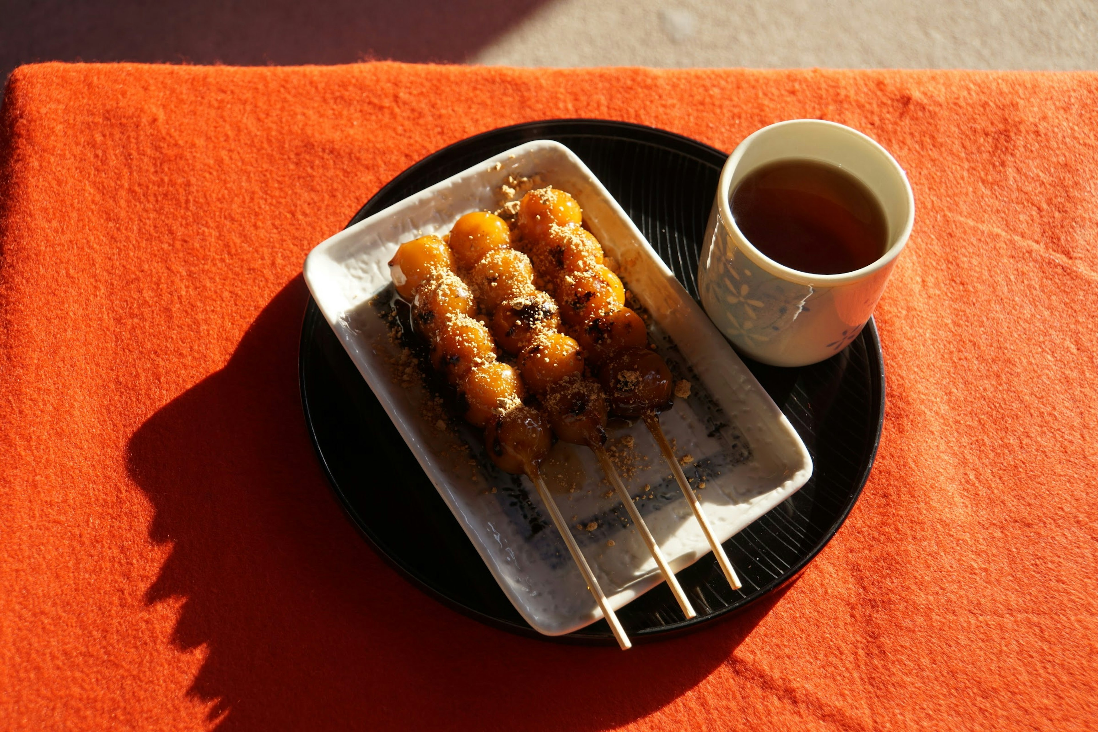 Comida en brochetas servida en un plato con té sobre un mantel naranja