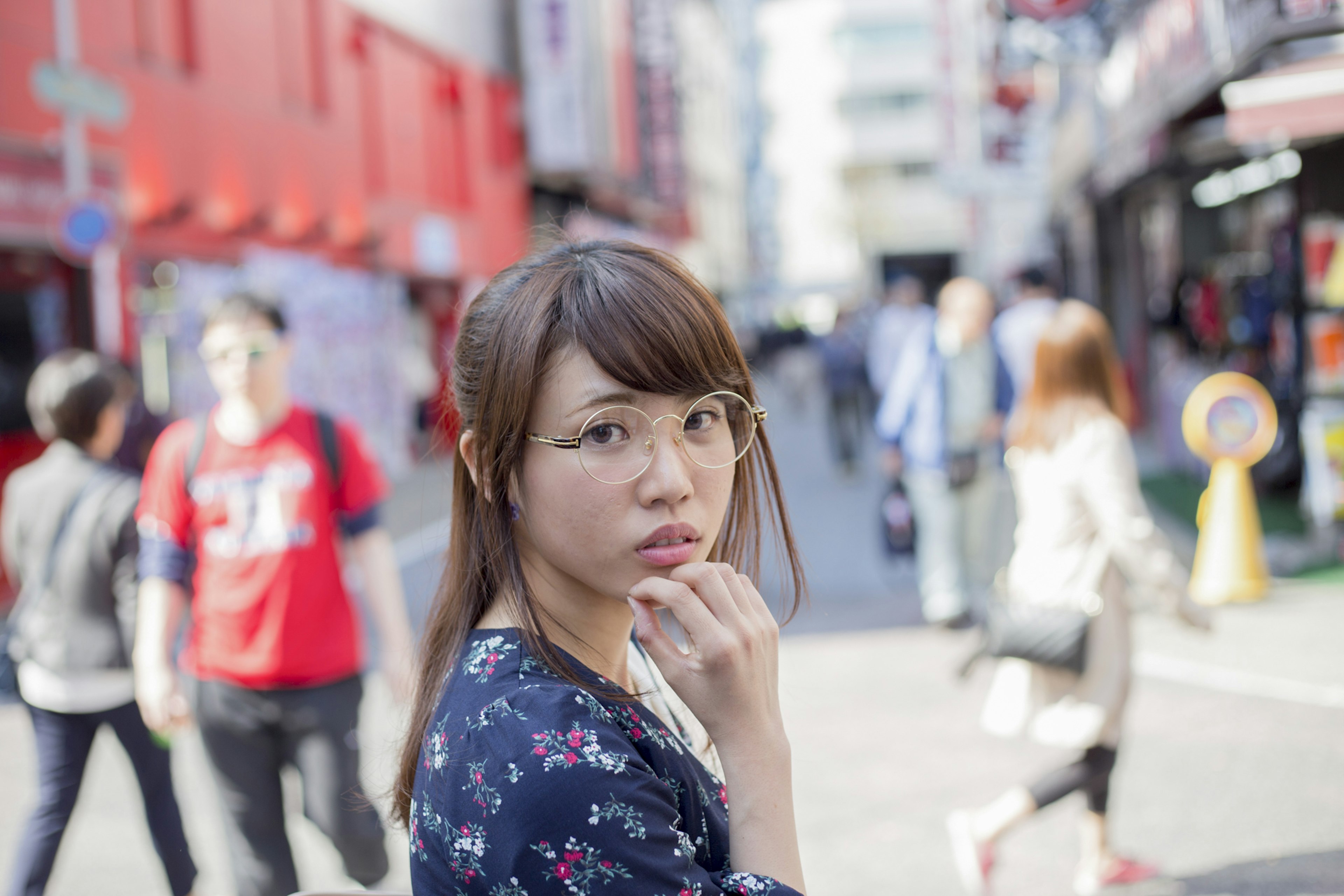 Una mujer volviéndose en la calle usando gafas y un vestido floral Fondo con edificios coloridos y personas caminando