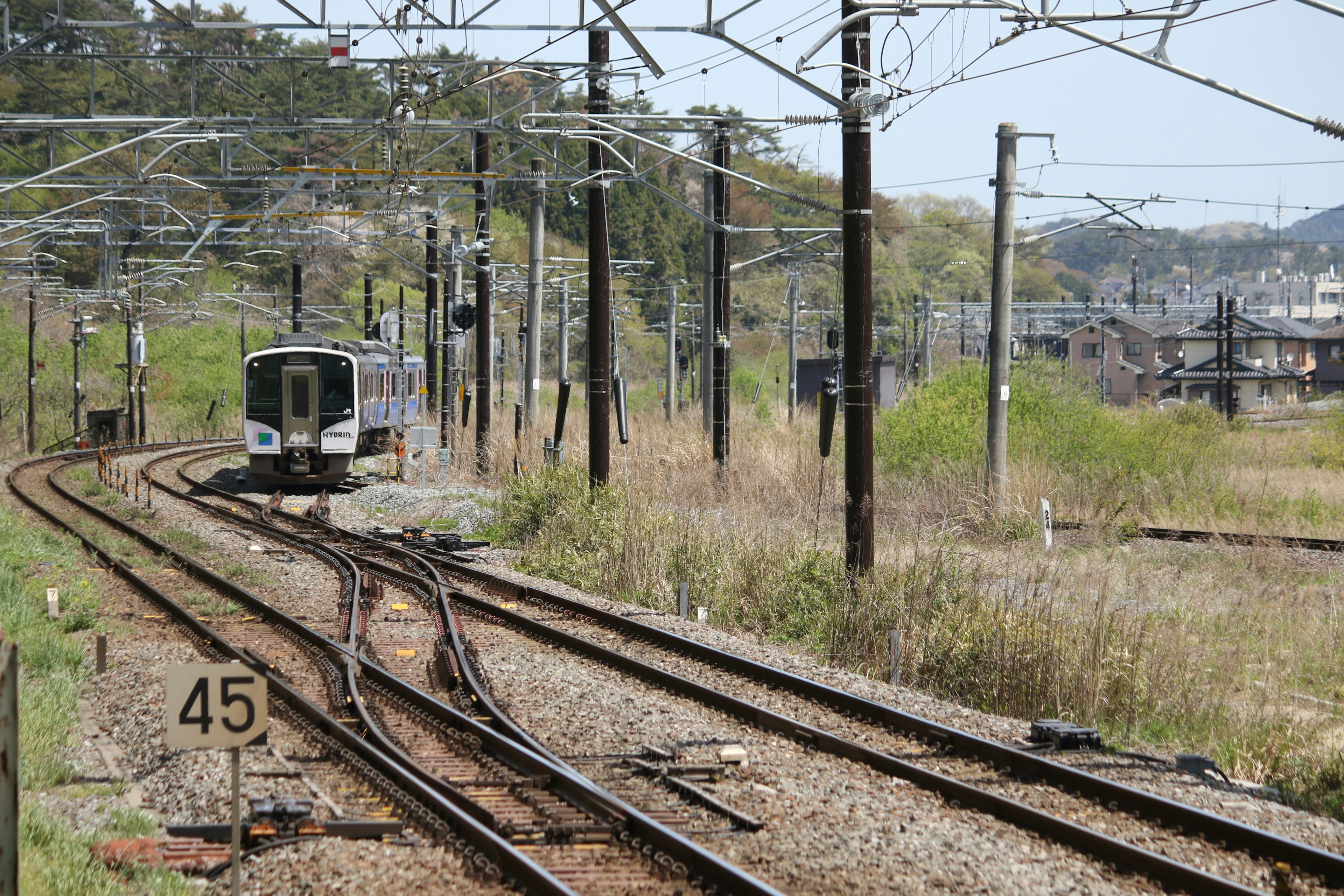 Kereta yang belok dengan rel dan tiang listrik di sekitarnya