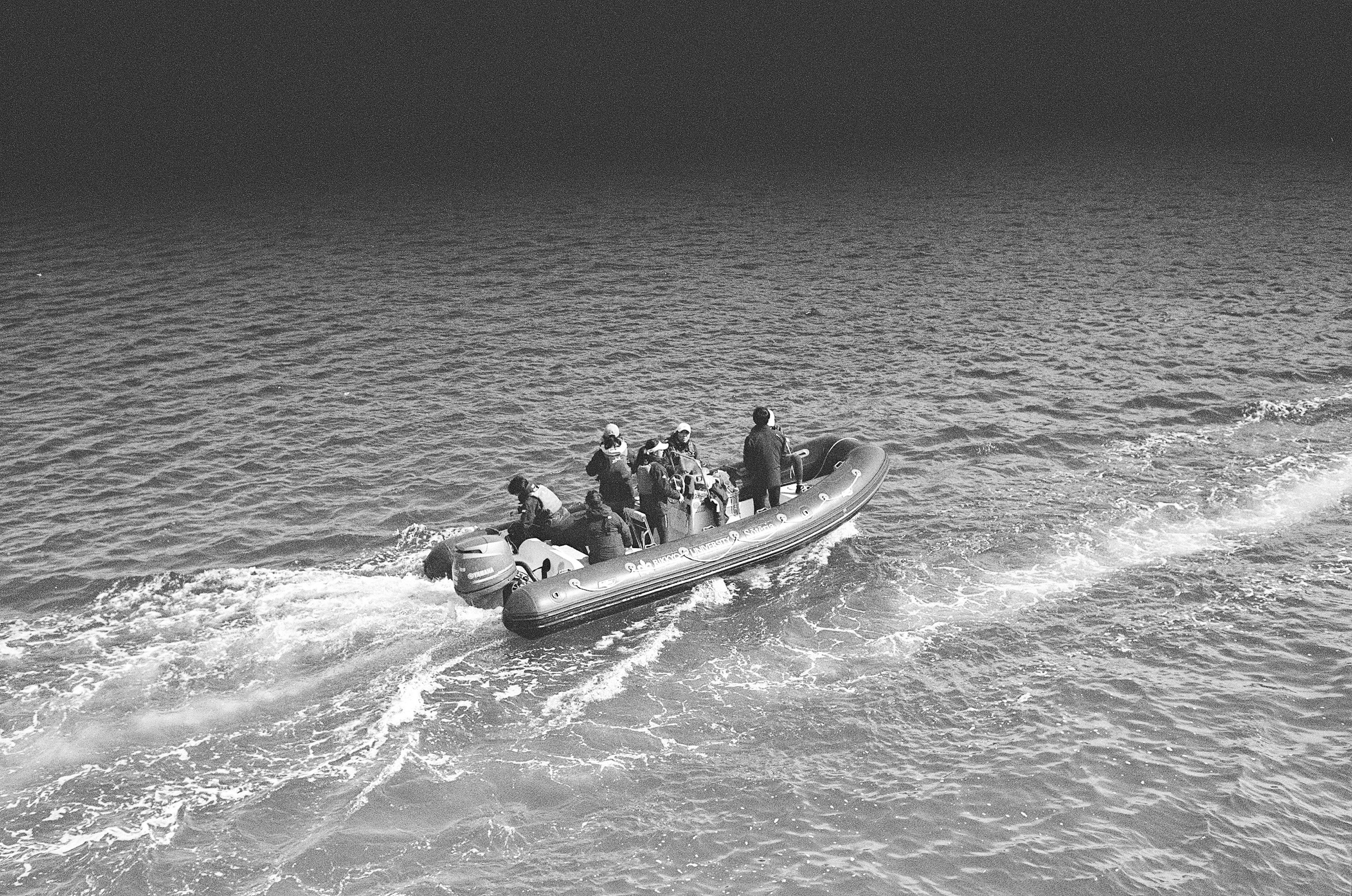 Image en noir et blanc d'un bateau naviguant sur la mer avec des personnes à bord