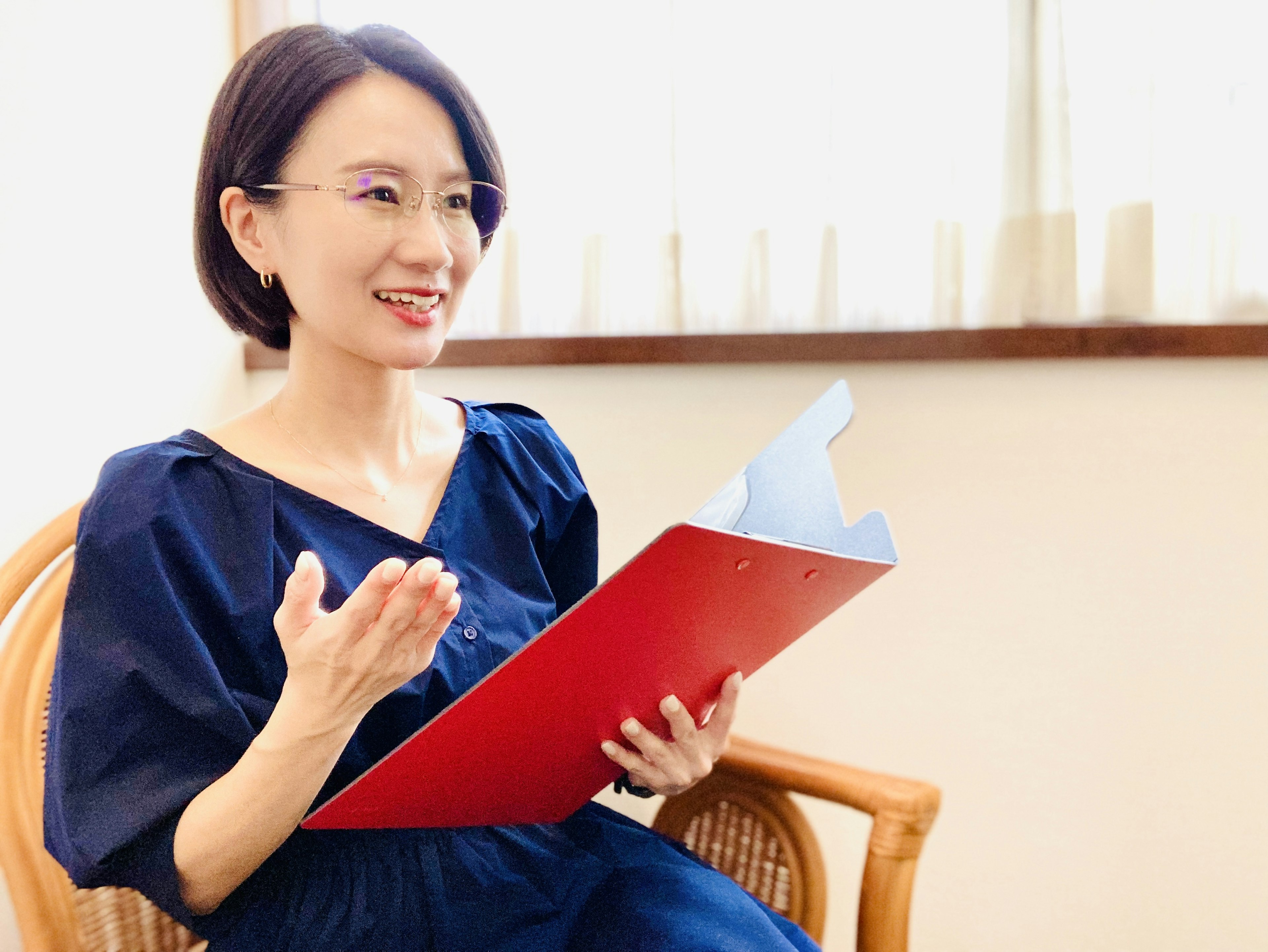 Smiling woman holding a red folder sitting on a chair