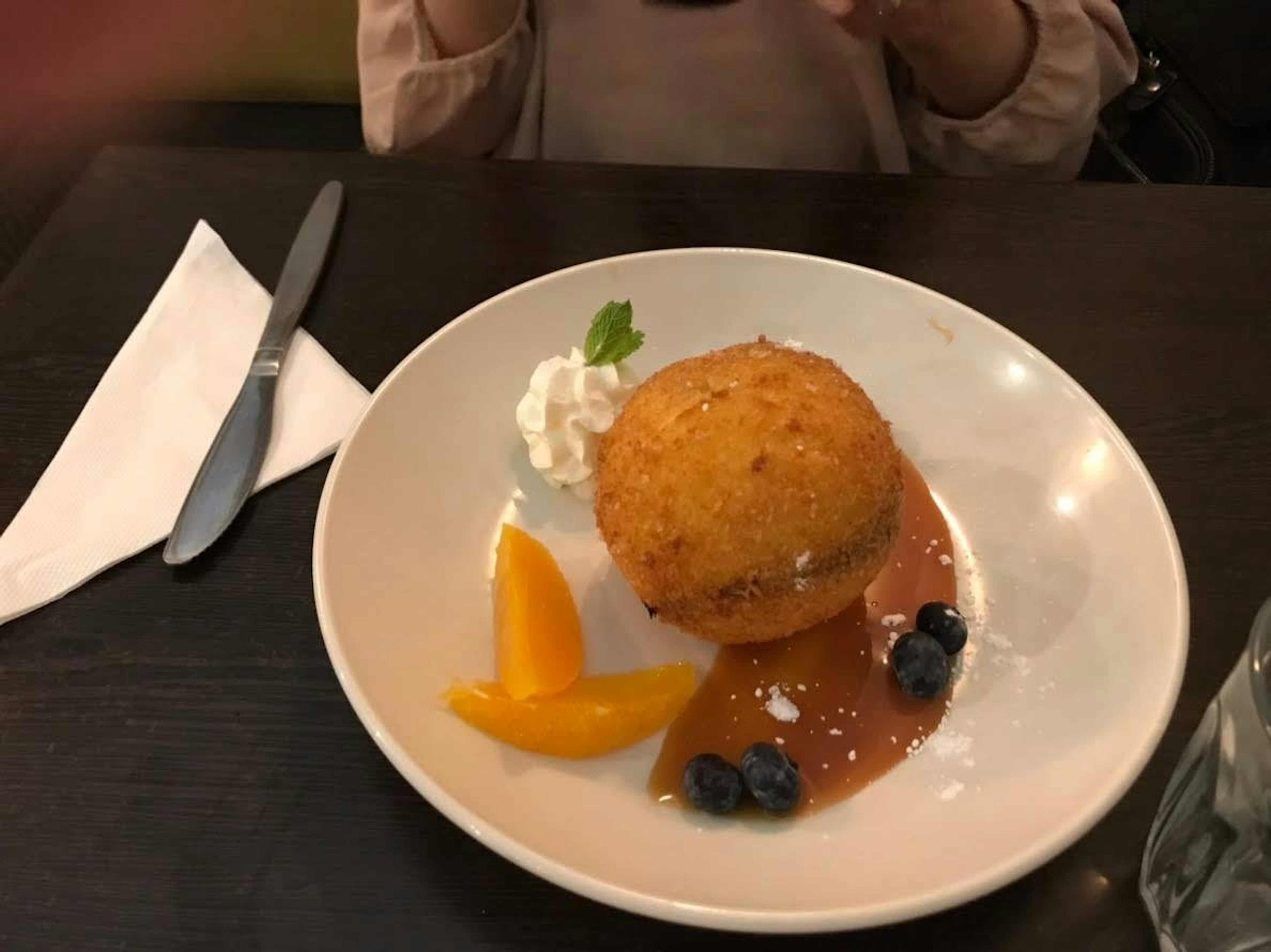 Bola de postre frita cubierta con crema y servida con rodajas de fruta en un plato blanco