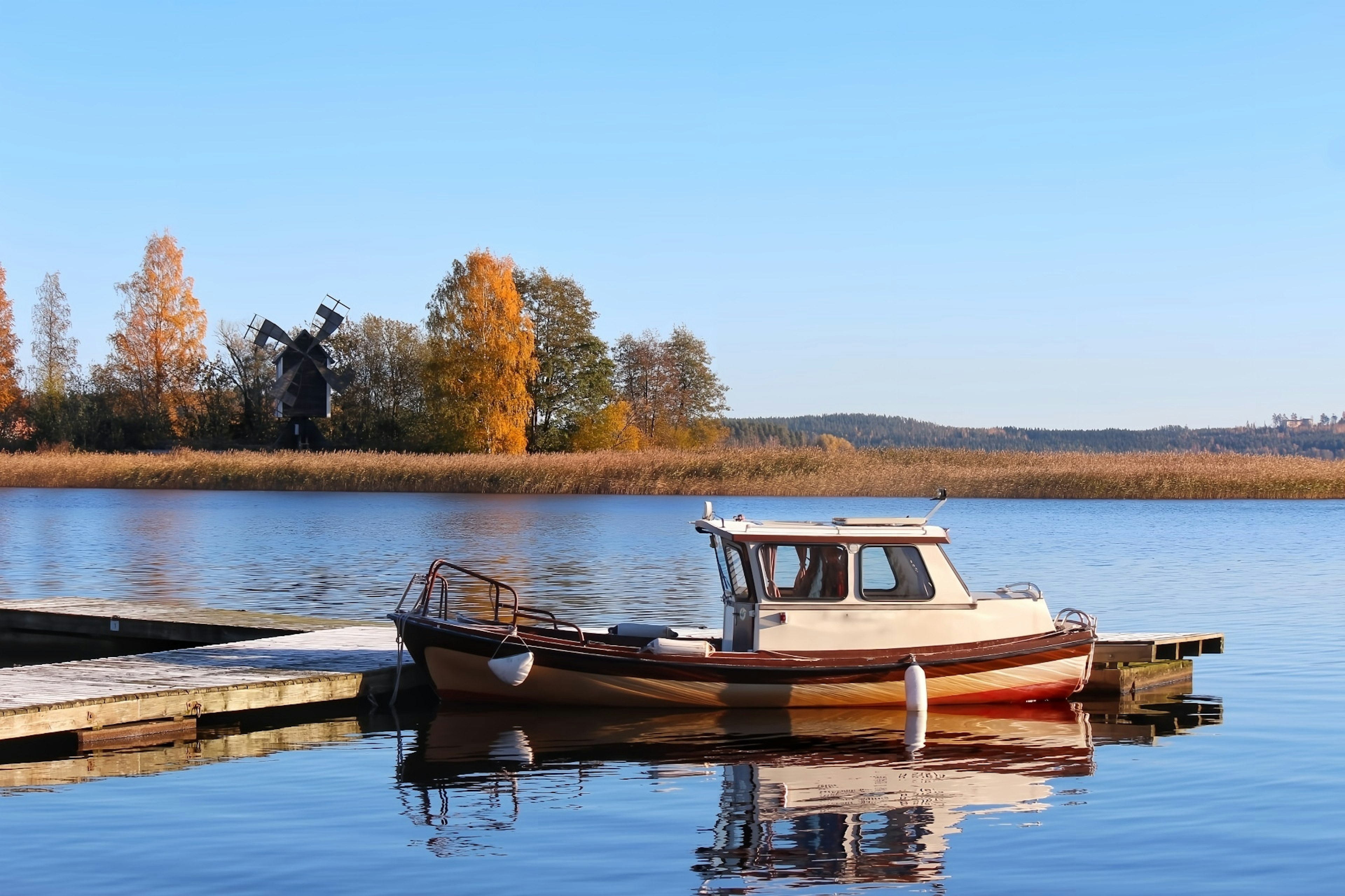 A small boat docked at a serene lake with autumn trees in the background