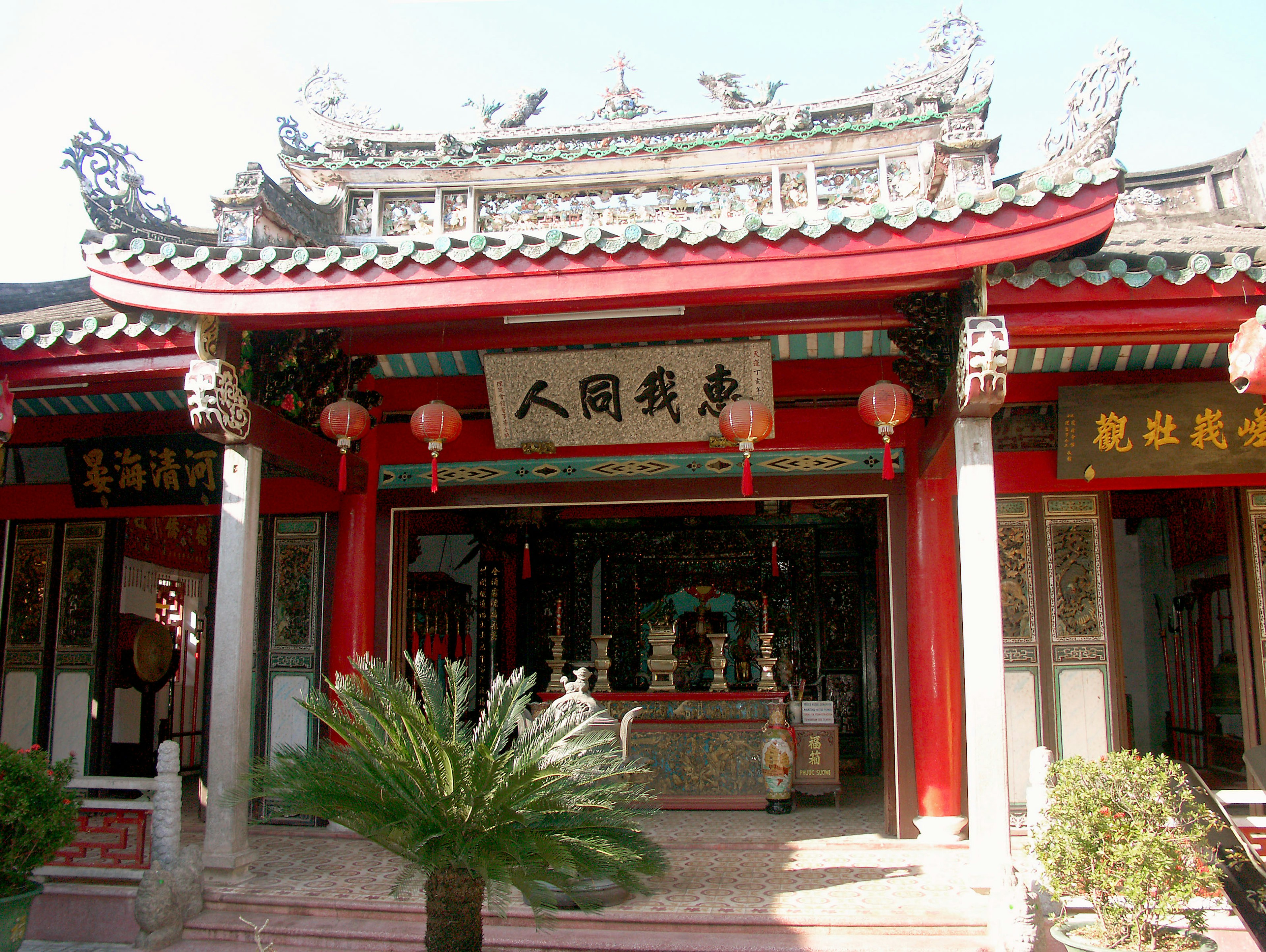 Traditional temple exterior with red roof featuring red lanterns and green plants