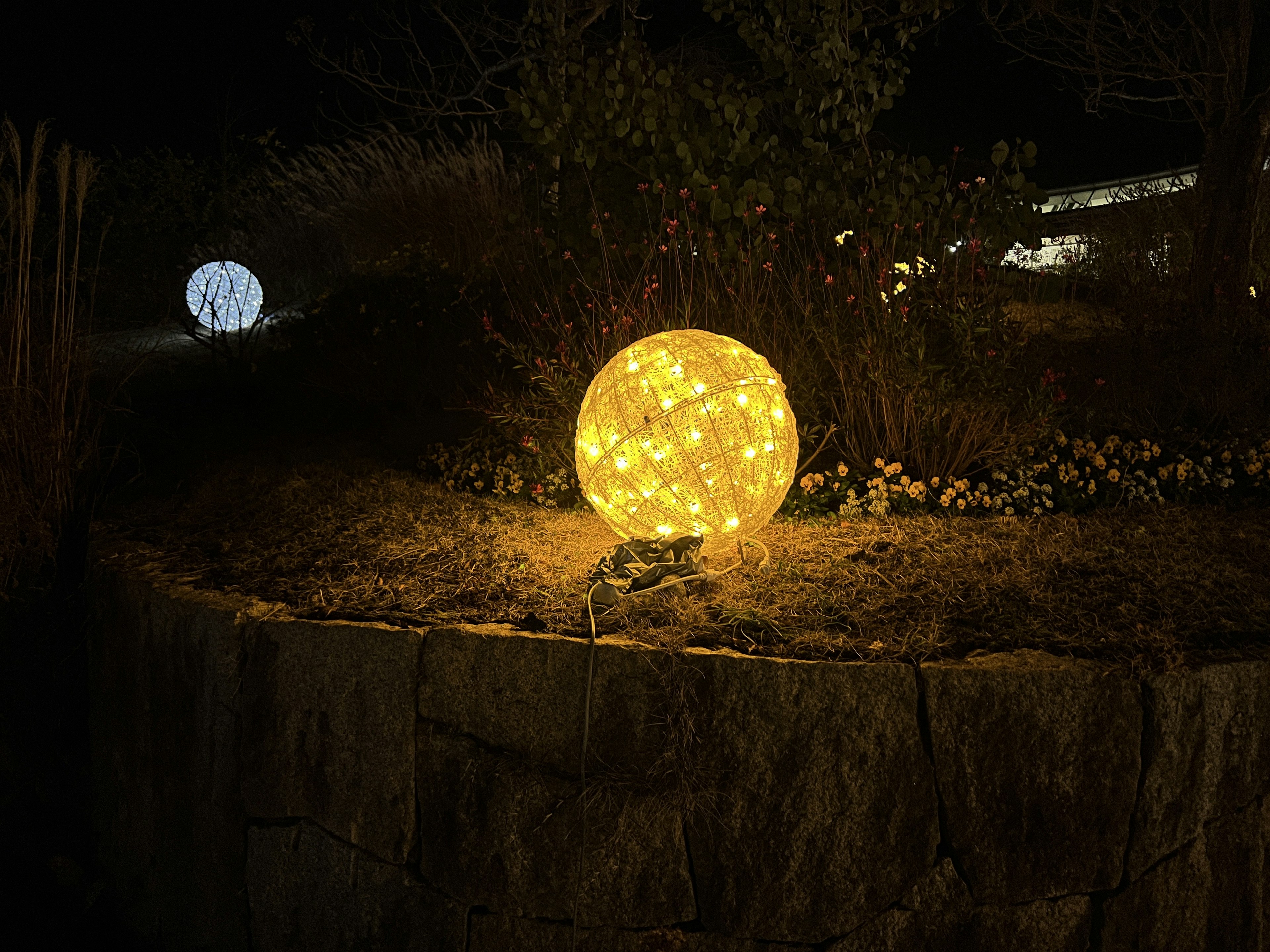 Eine leuchtende gelbe Lichtkugel in einem Nachgarten mit einer blauen Lichtkugel im Hintergrund