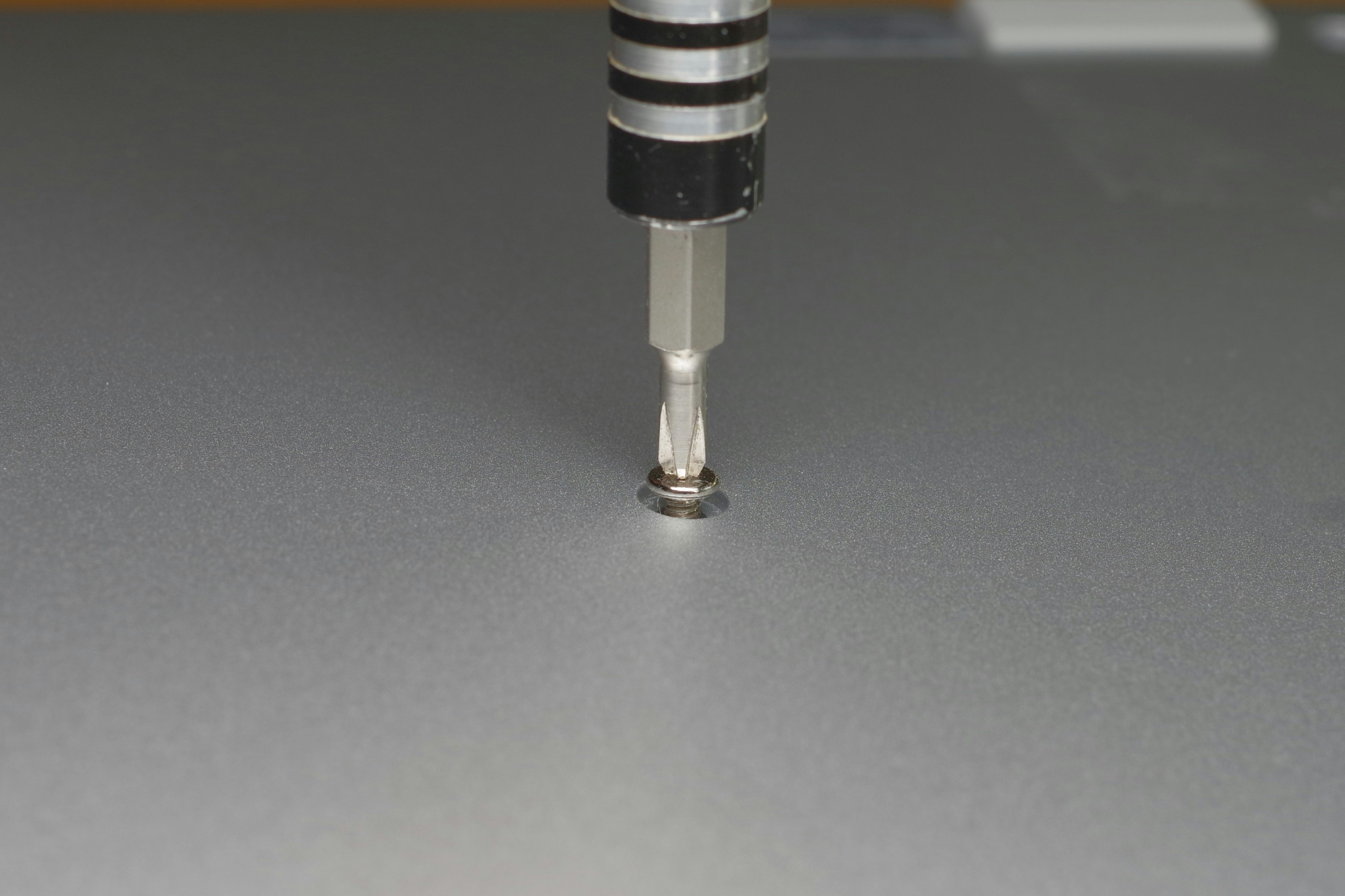 Close-up of a screw and screwdriver on a silver metal surface