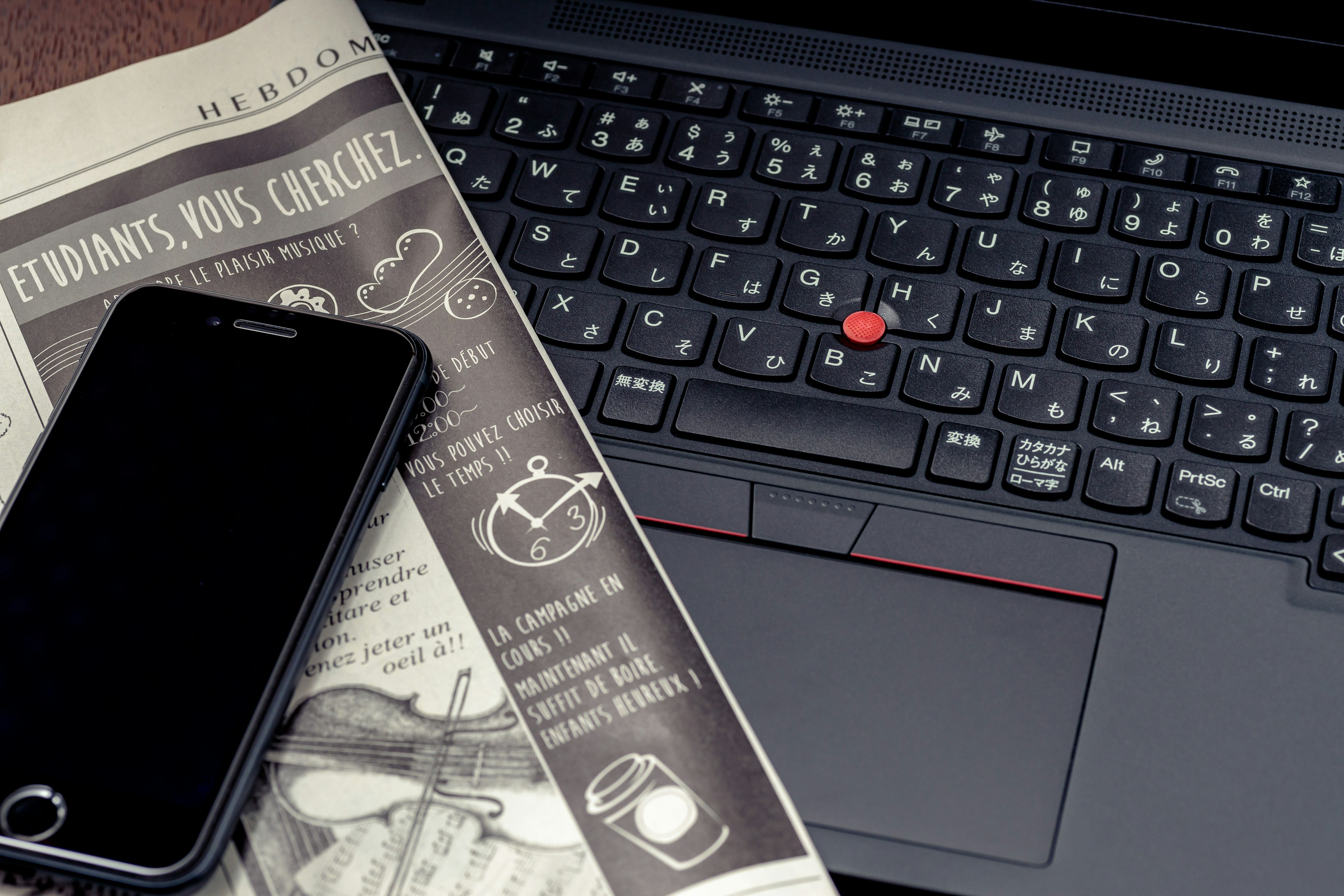 Laptop keyboard with a black smartphone and a newspaper