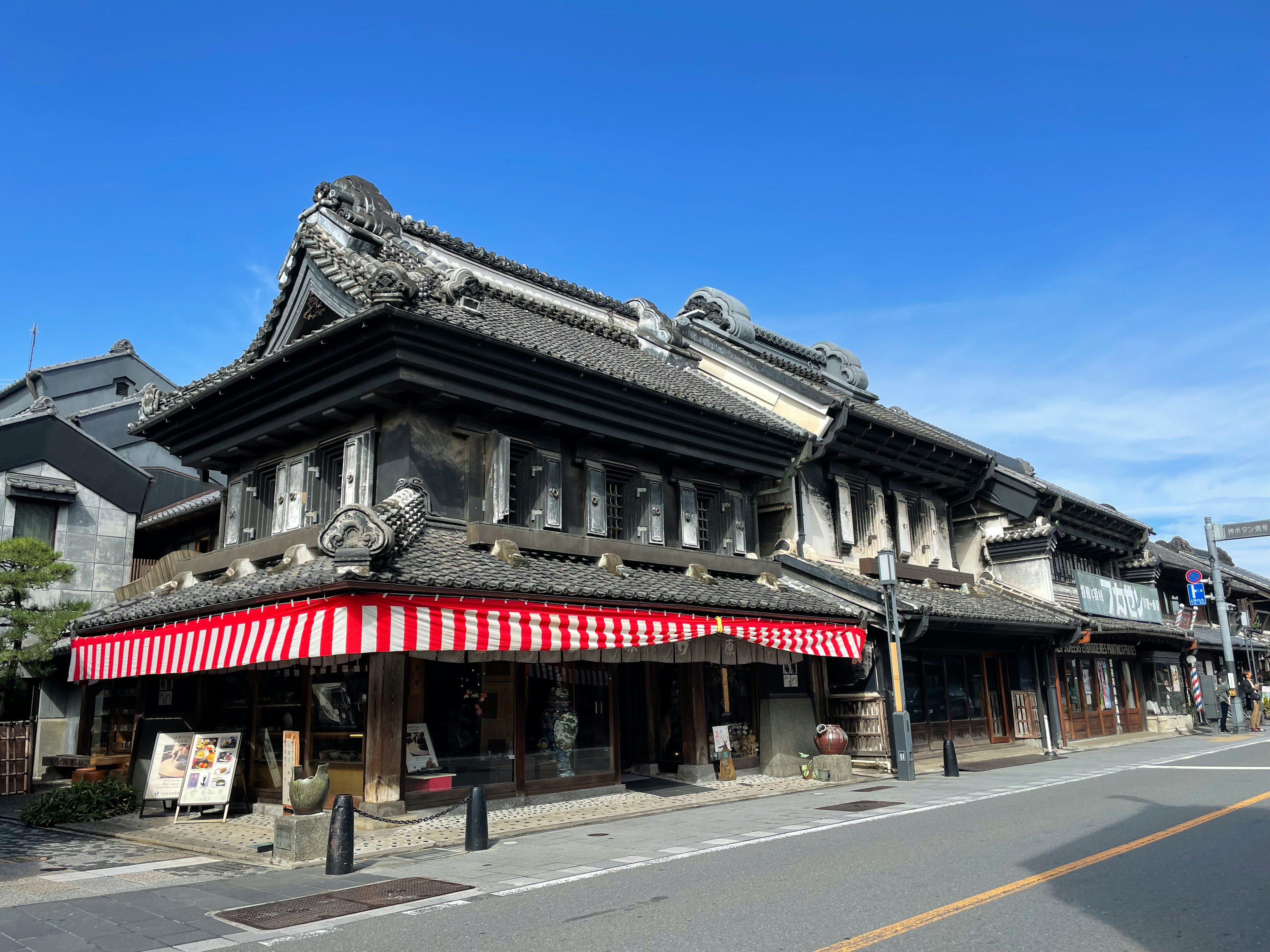 伝統的な日本建築の商店街の外観赤と白のストライプのテントの下に店舗が並ぶ青空の背景