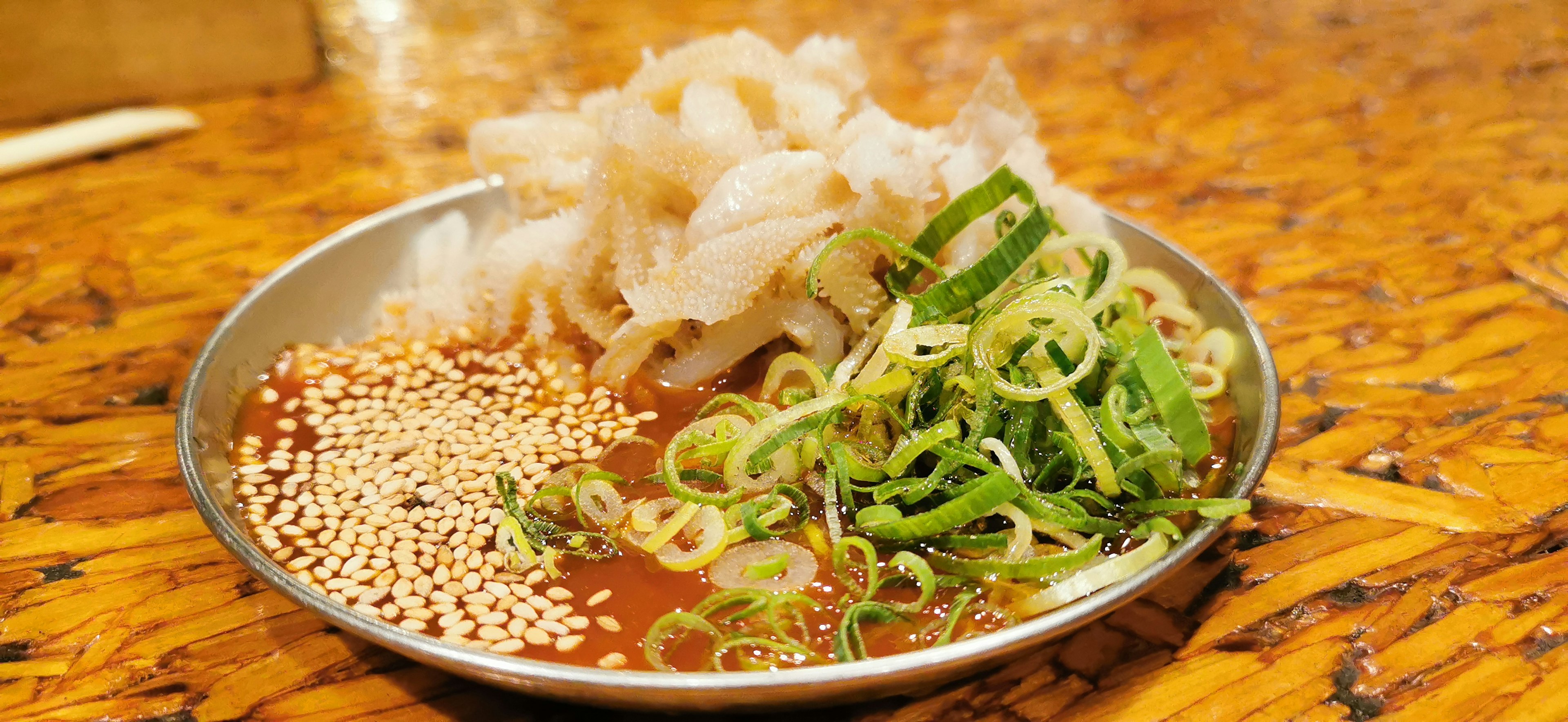 Un plato de sashimi con pescado en rodajas cebollas verdes y semillas de sésamo