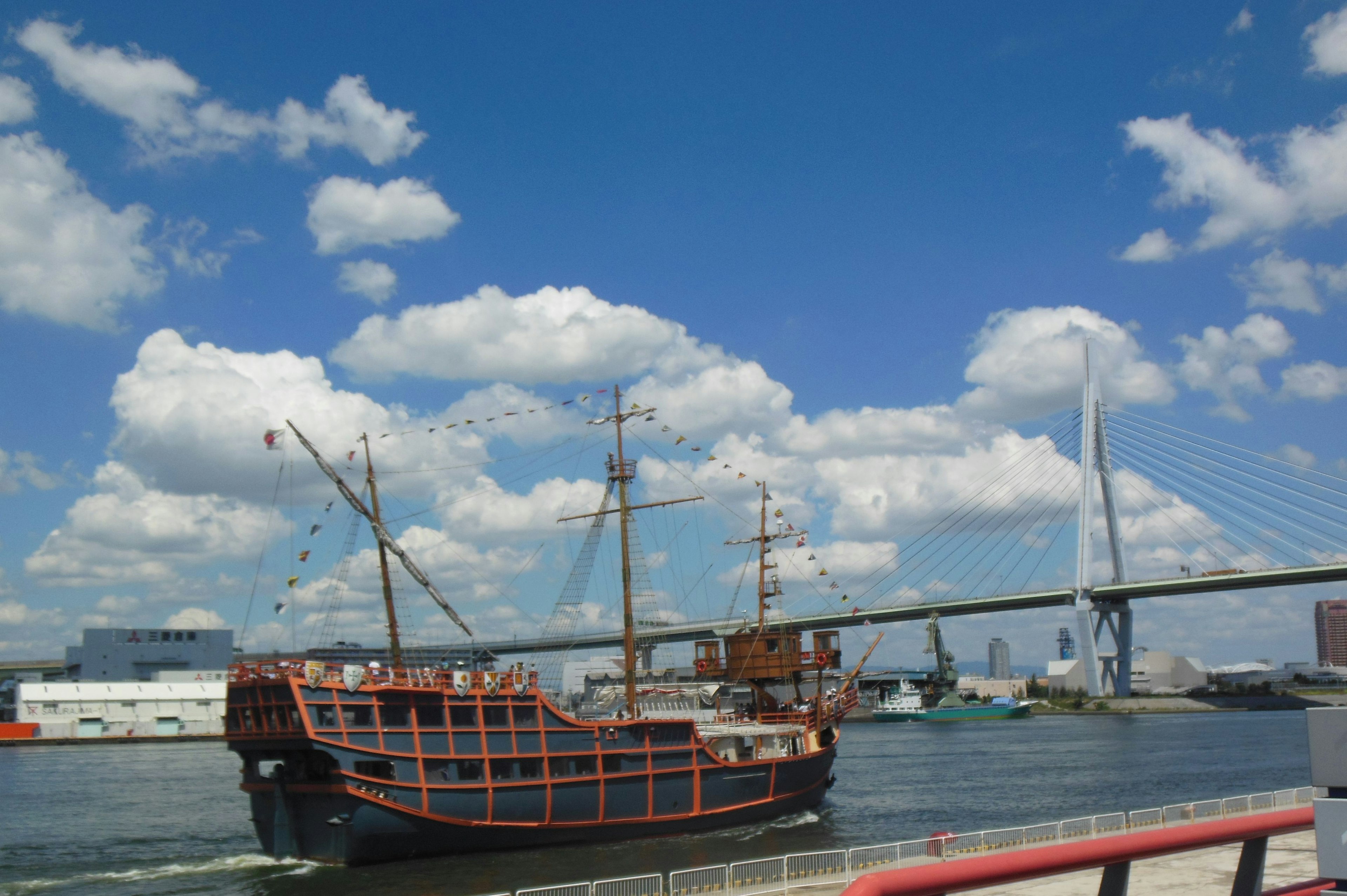 เรือใบดั้งเดิมใต้ท้องฟ้าสีฟ้าพร้อมเมฆและสะพานสมัยใหม่