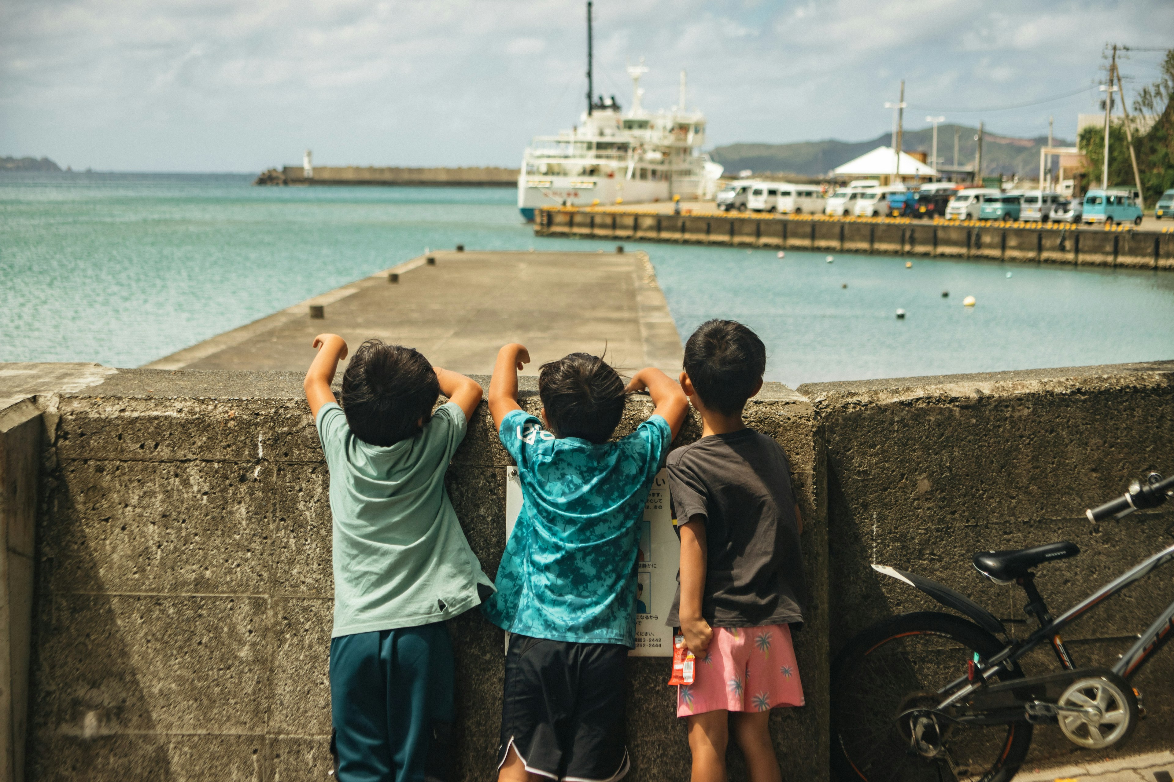 Kinder lehnen sich an einen Pier und schauen auf ein Boot im Hafen