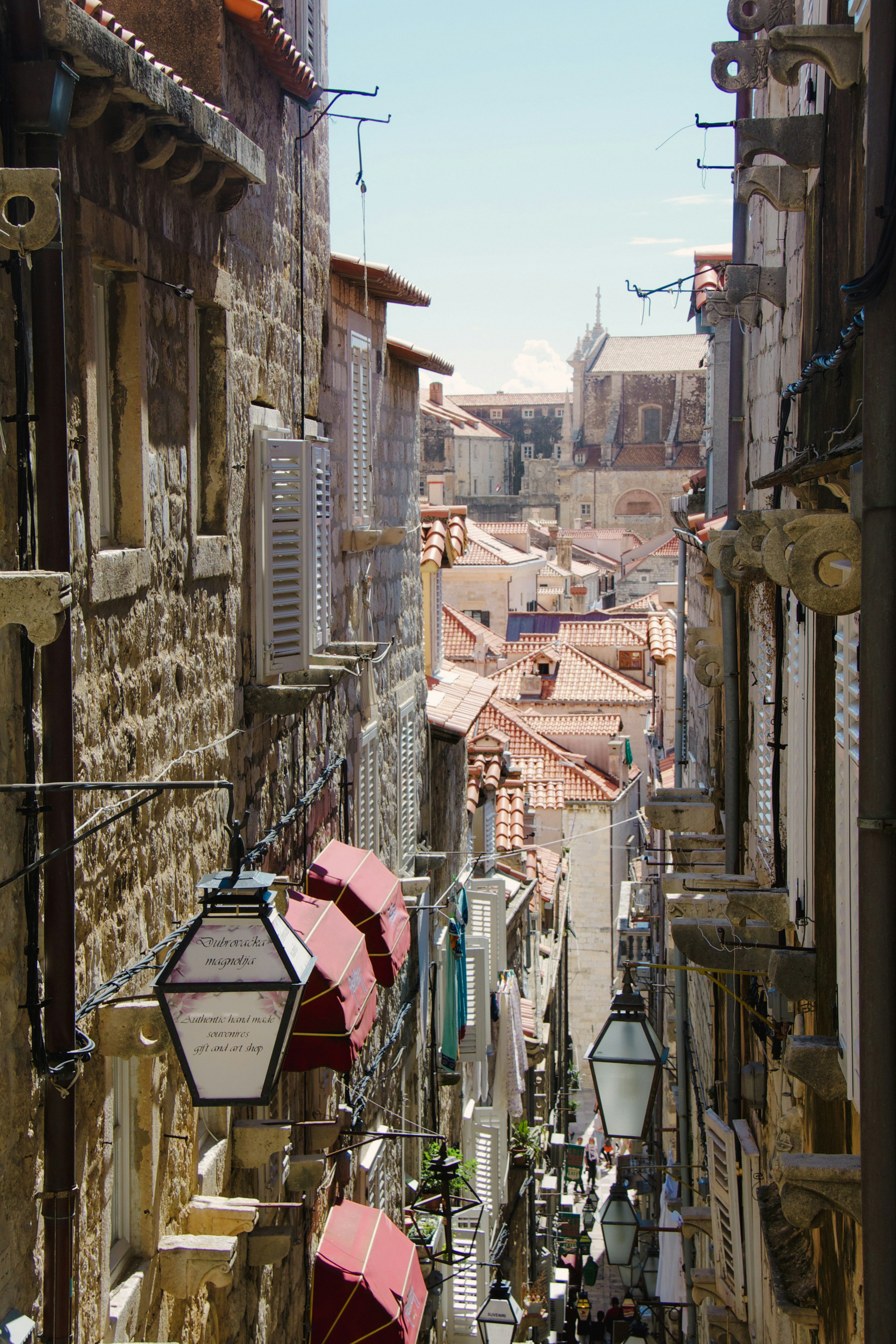 Calle estrecha de piedra flanqueada por faroles y edificios con techos rojos