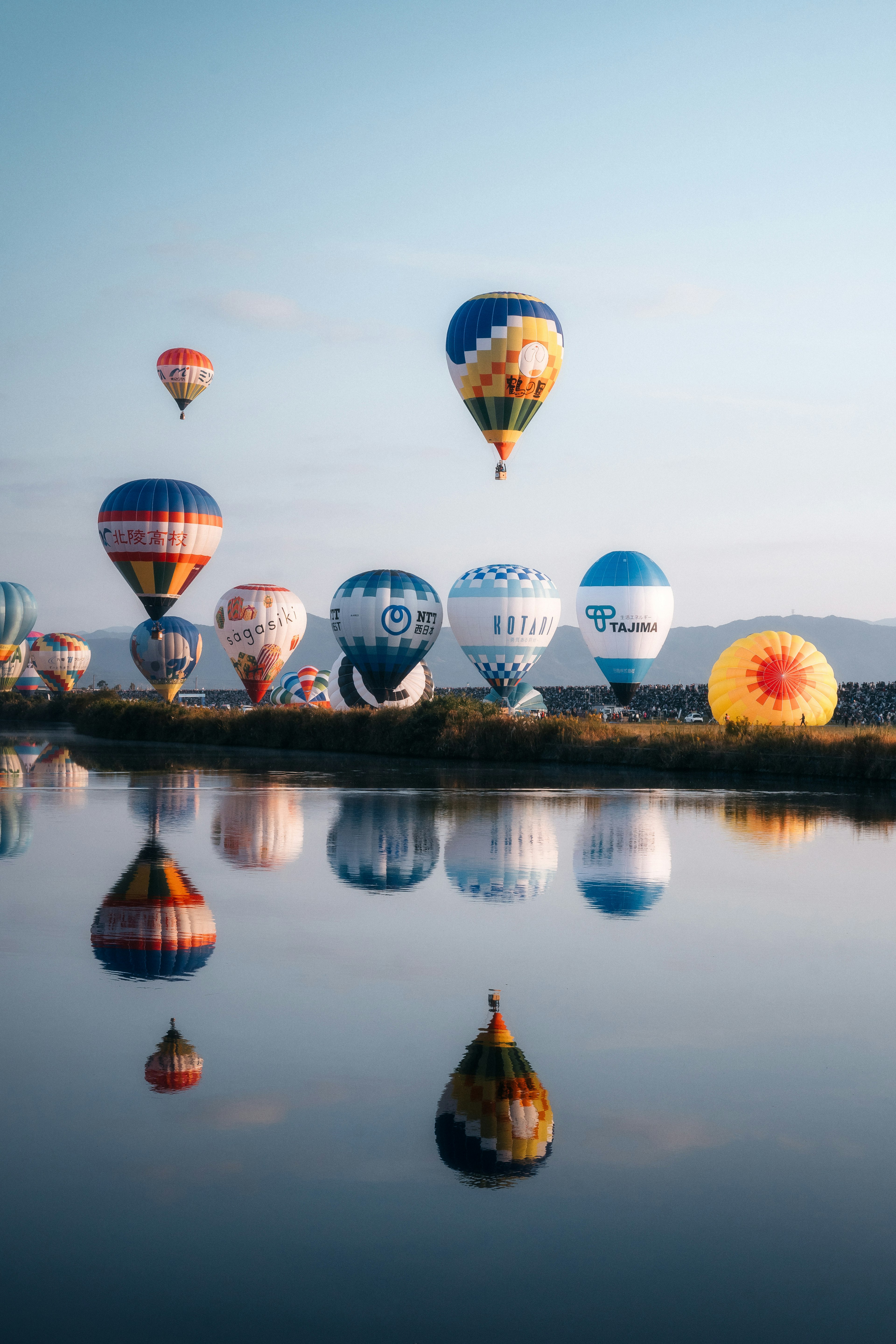 Globos de aire caliente coloridos flotando bajo un cielo azul con reflejos en el agua