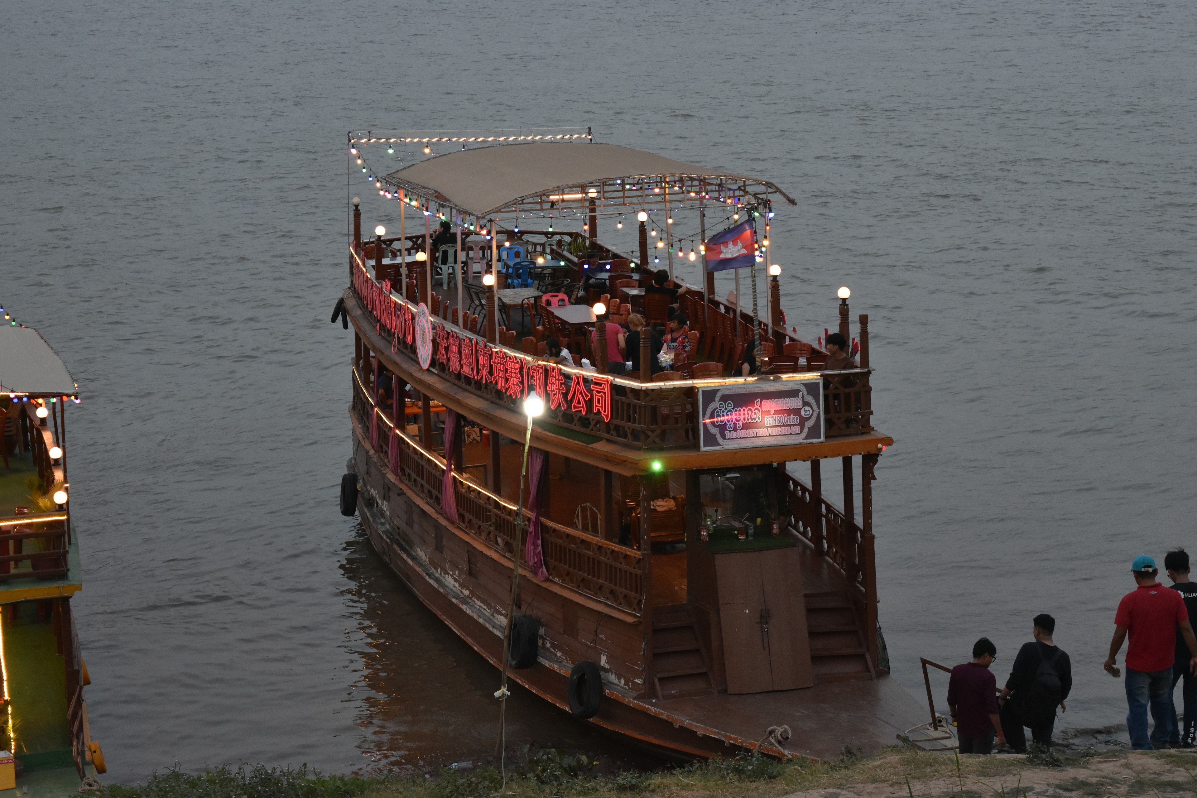 Scène nocturne d'un bateau touristique en bois sur la rivière avec des personnes embarquant