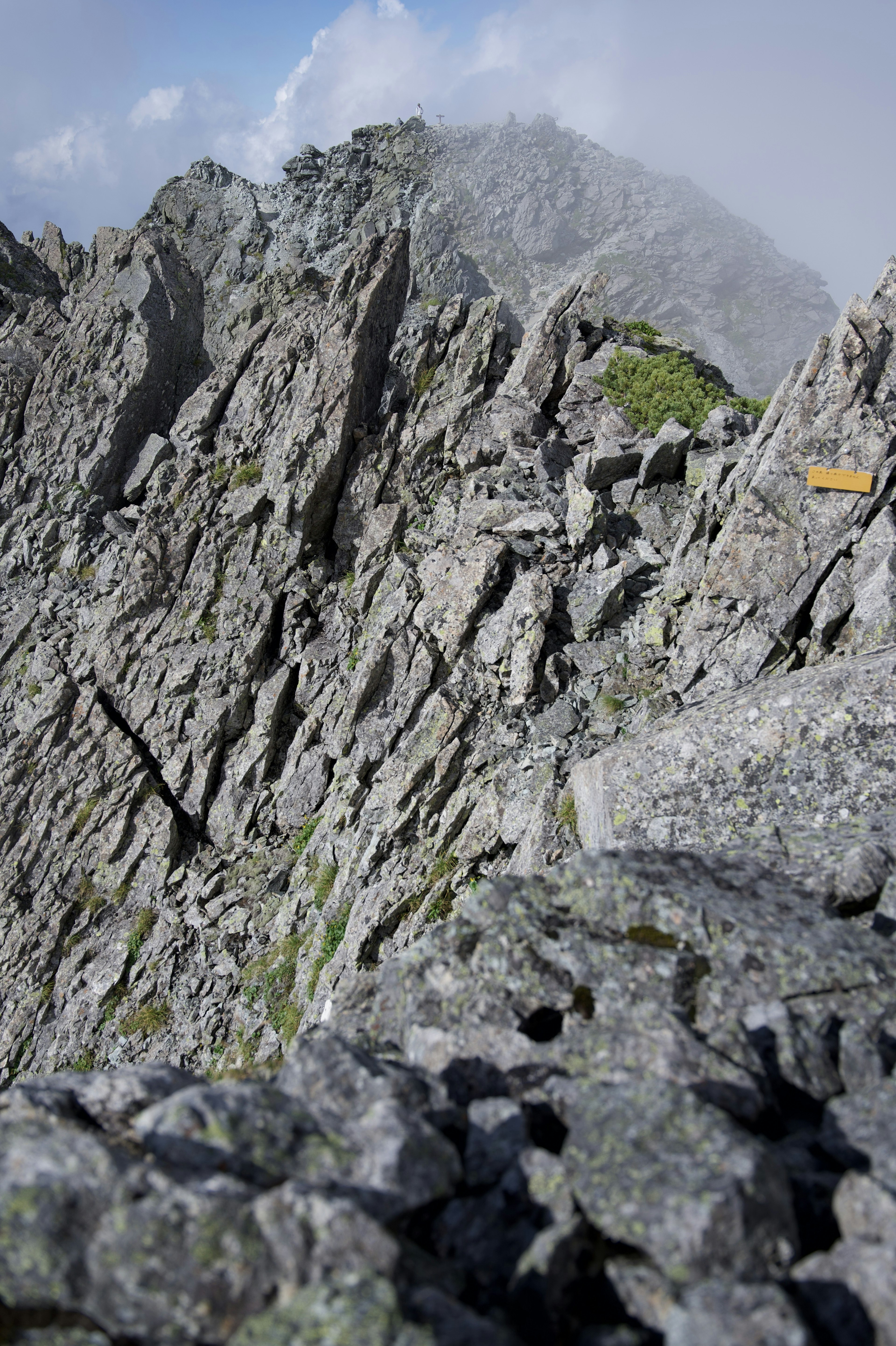 Paesaggio montano impervio con scogliere rocciose e uno sfondo nuvoloso con erba verde