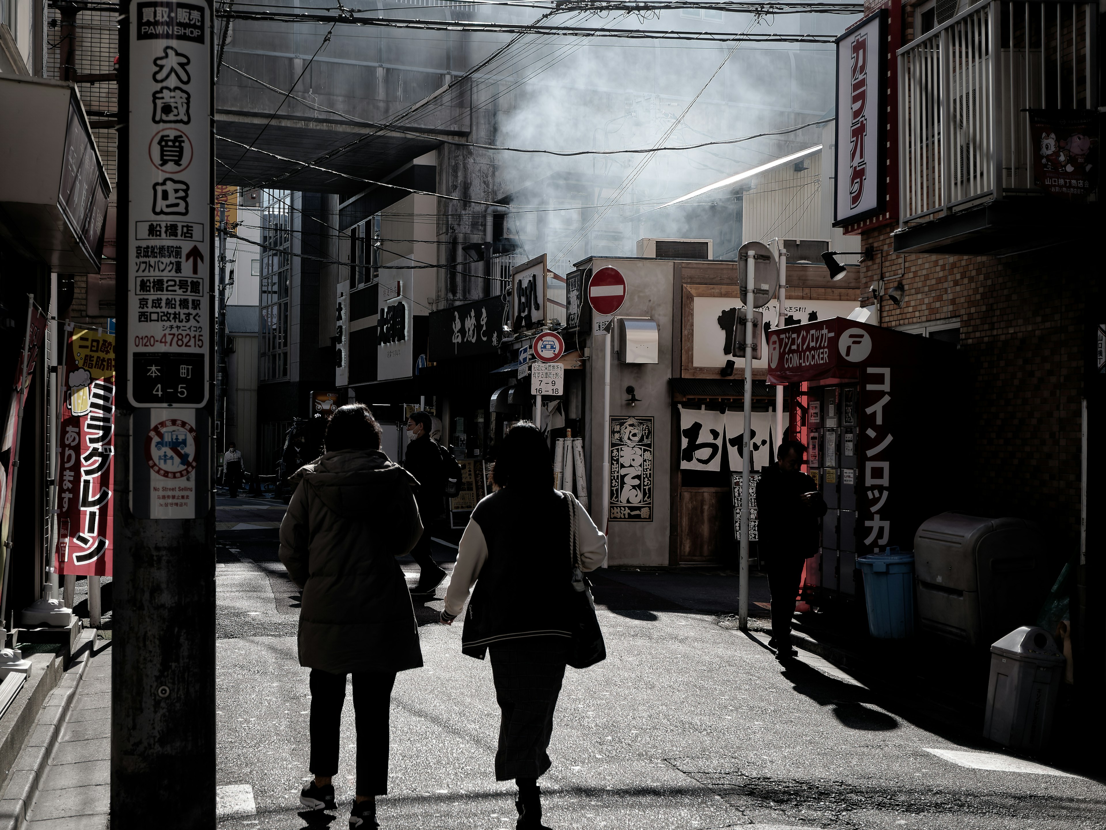 Two people walking in a Japanese street with smoke rising