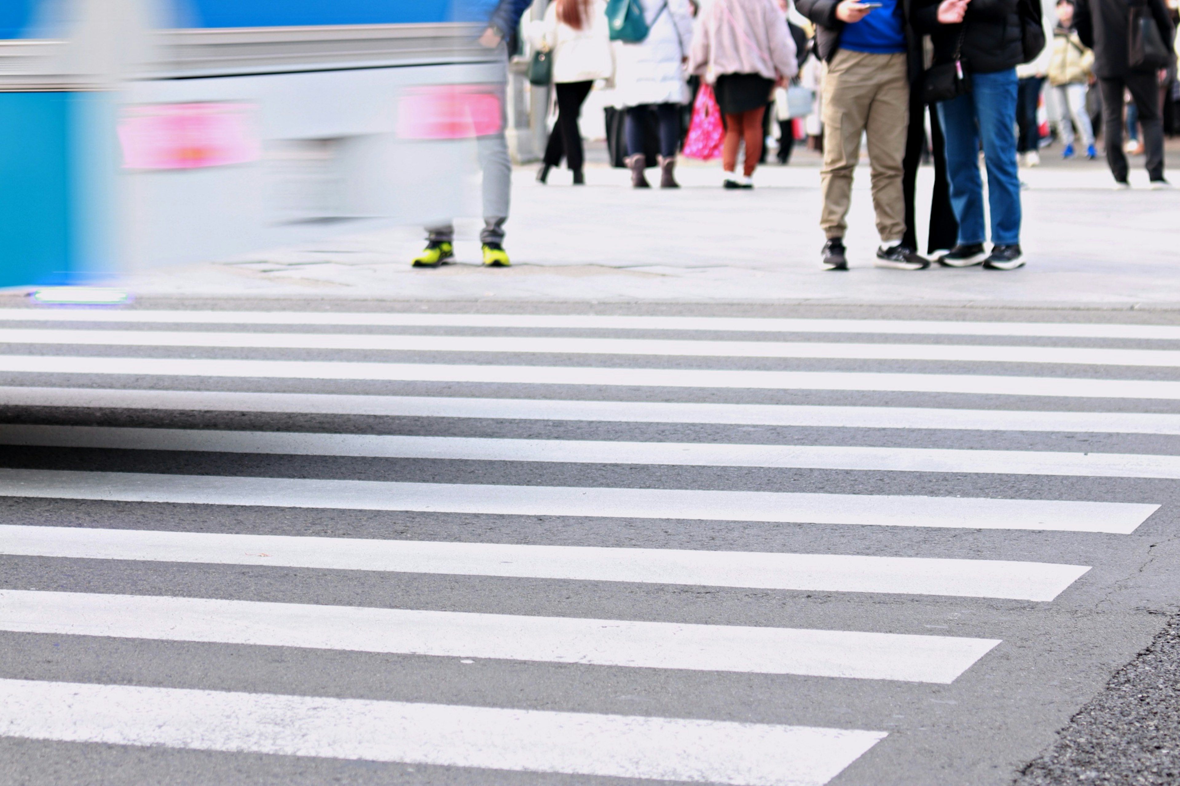 Una scena di strada con persone su un attraversamento pedonale bianco e un veicolo blu in movimento