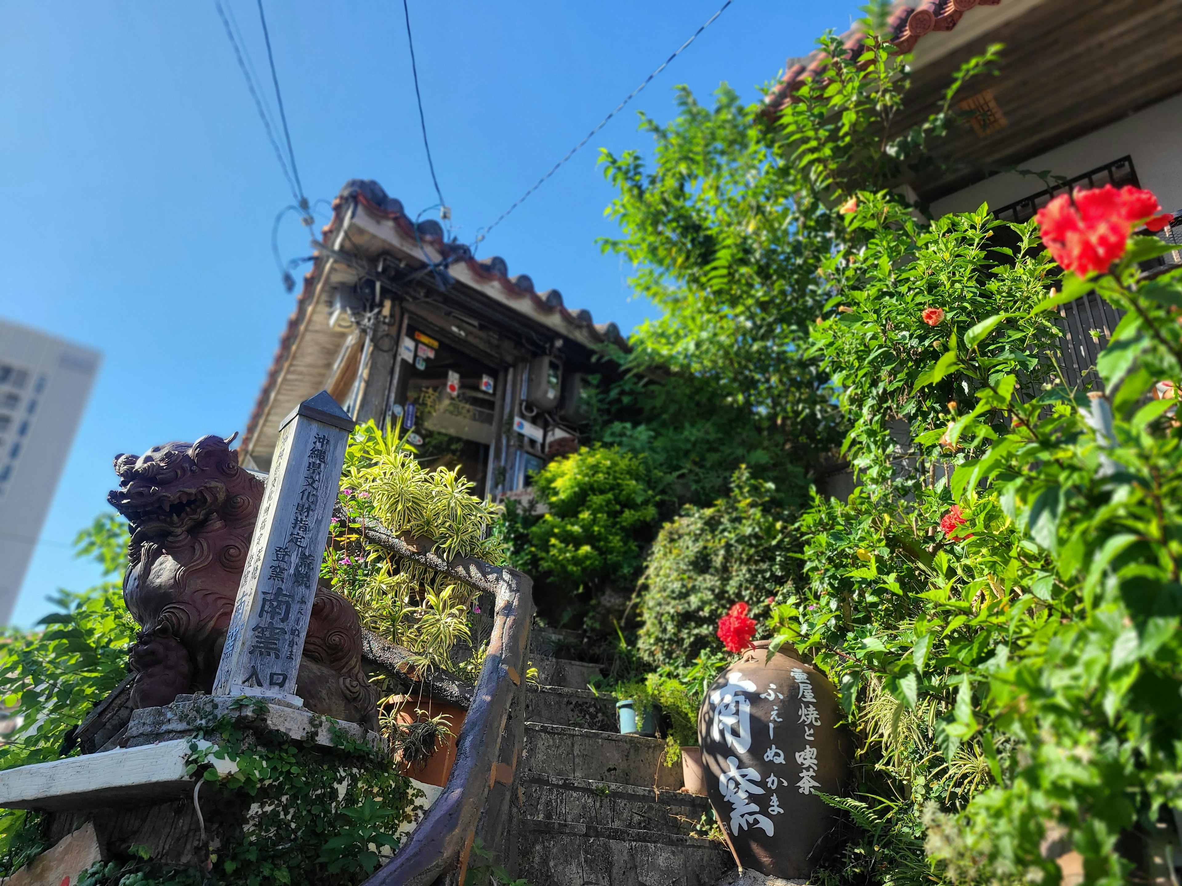 Traditionelles Haus umgeben von Grün mit Steinstufen und roten Blumen