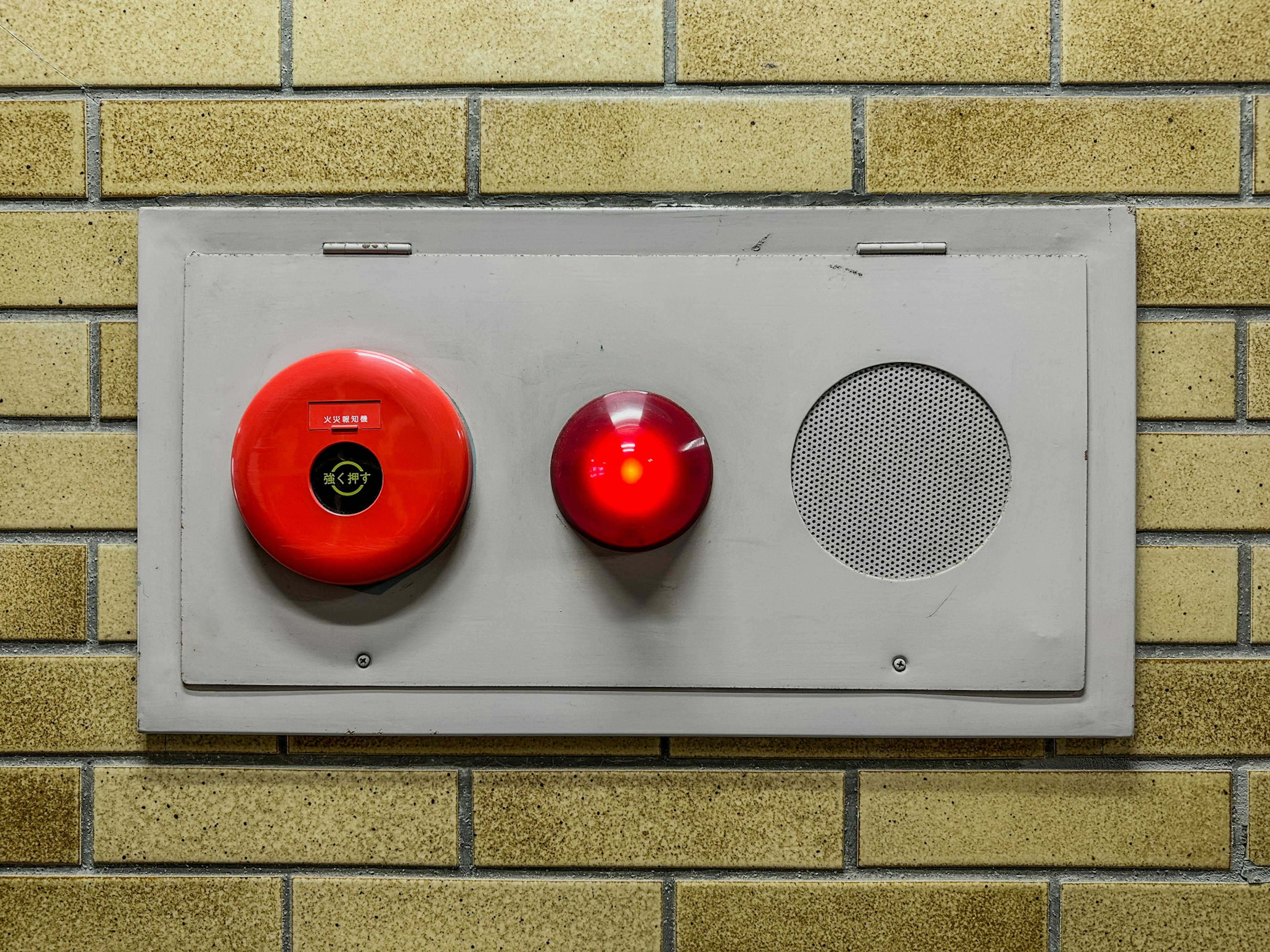 Panel gris con alarma contra incendios roja y luz montado en una pared de ladrillos