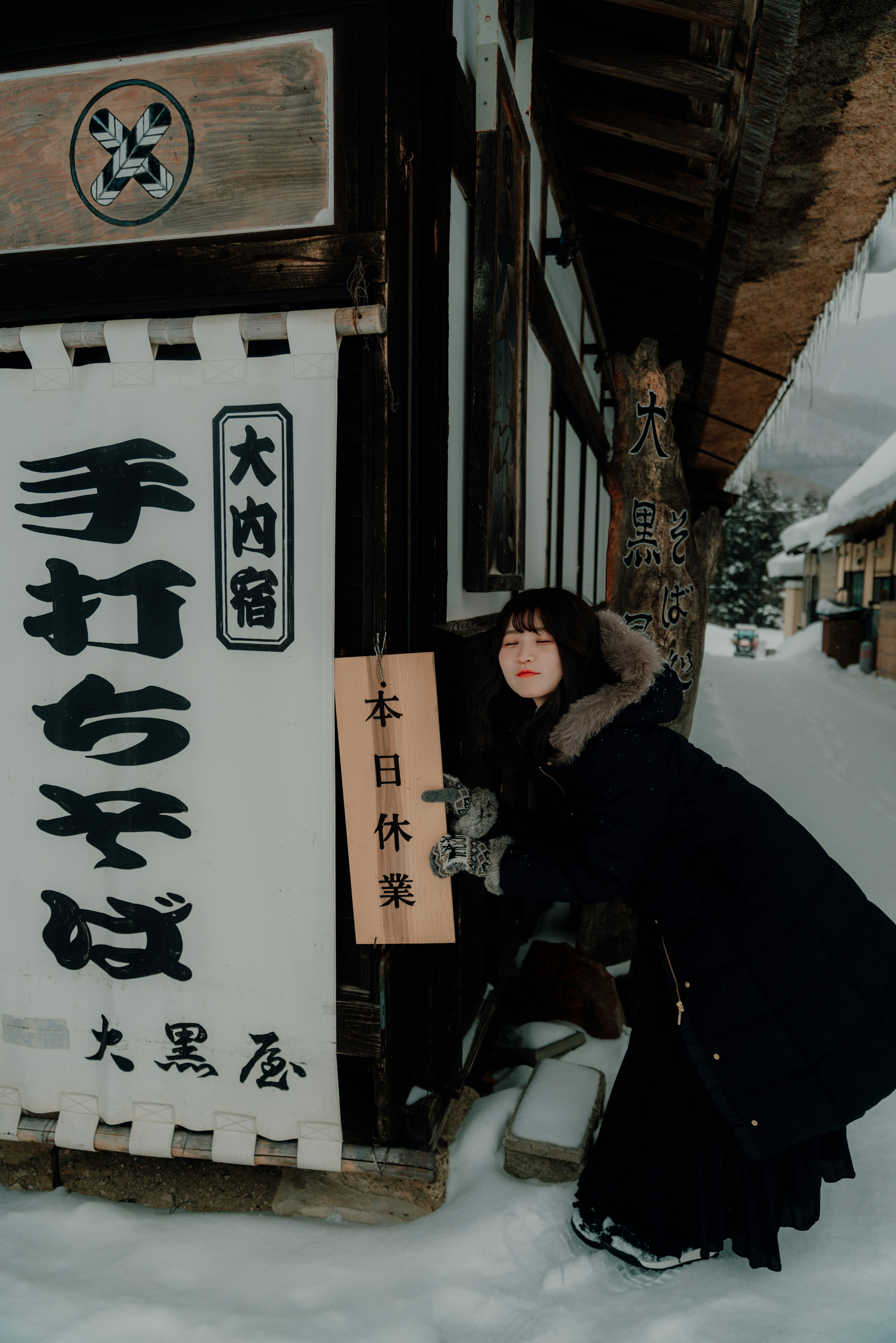 雪の中に立つ女性と伝統的な看板のある日本の街並み