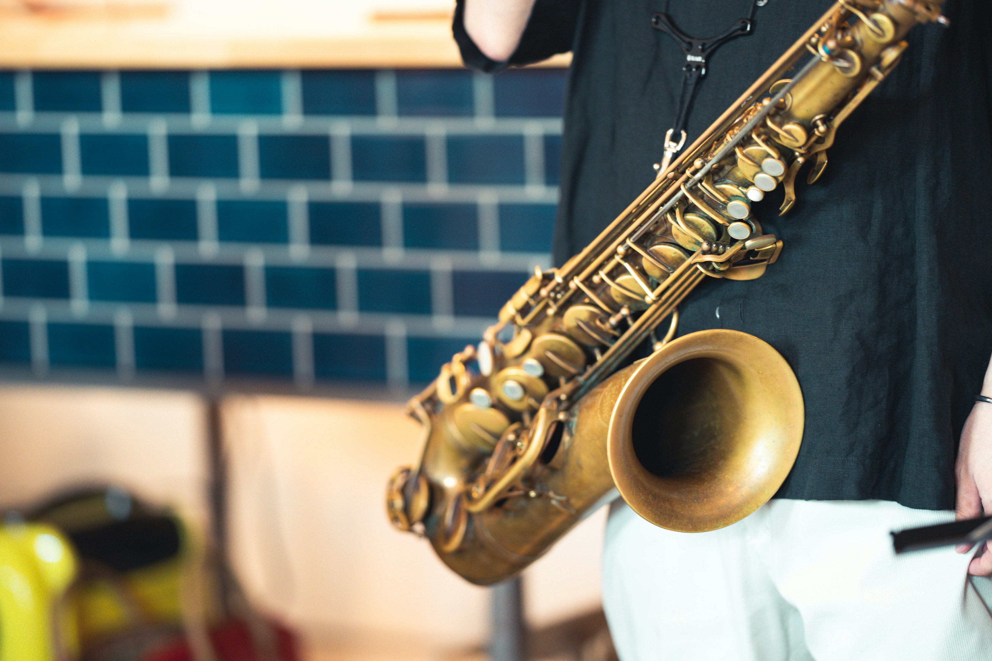 Close-up of a person holding a saxophone with a blue tiled background