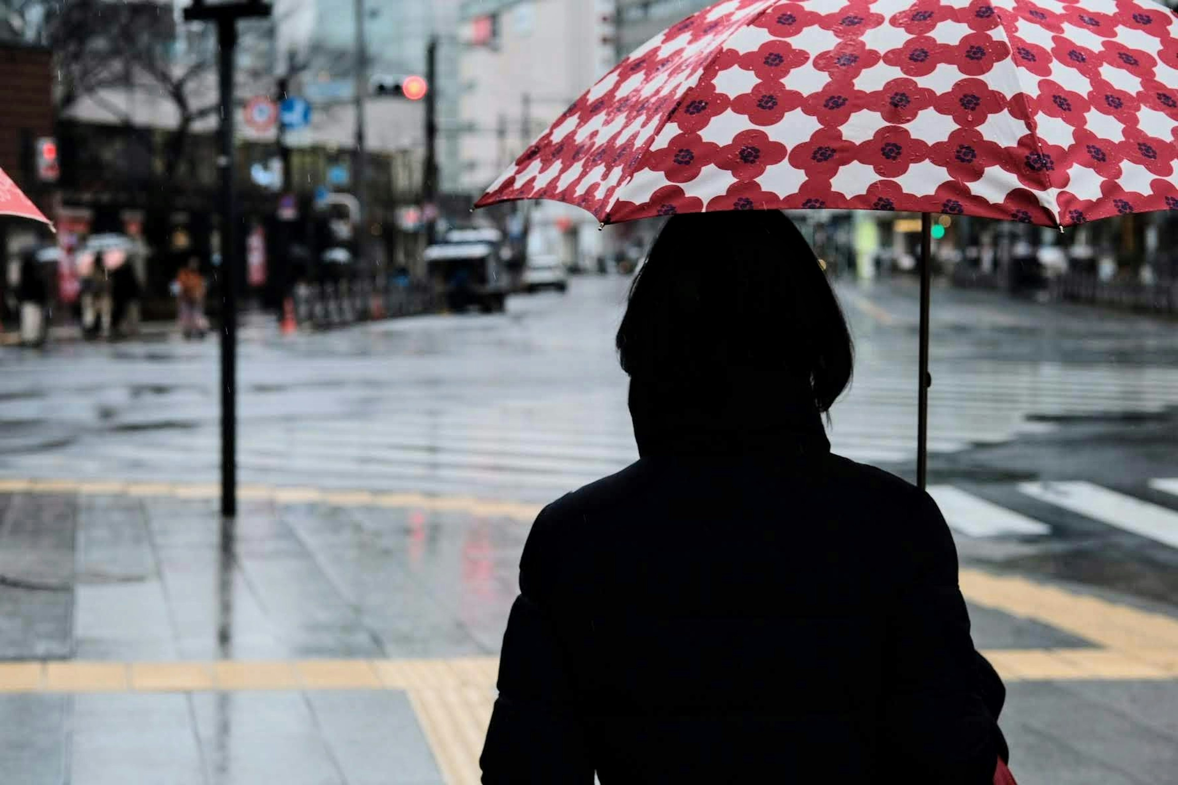 Une personne tenant un parapluie à carreaux rouges se tenant dans une scène urbaine pluvieuse