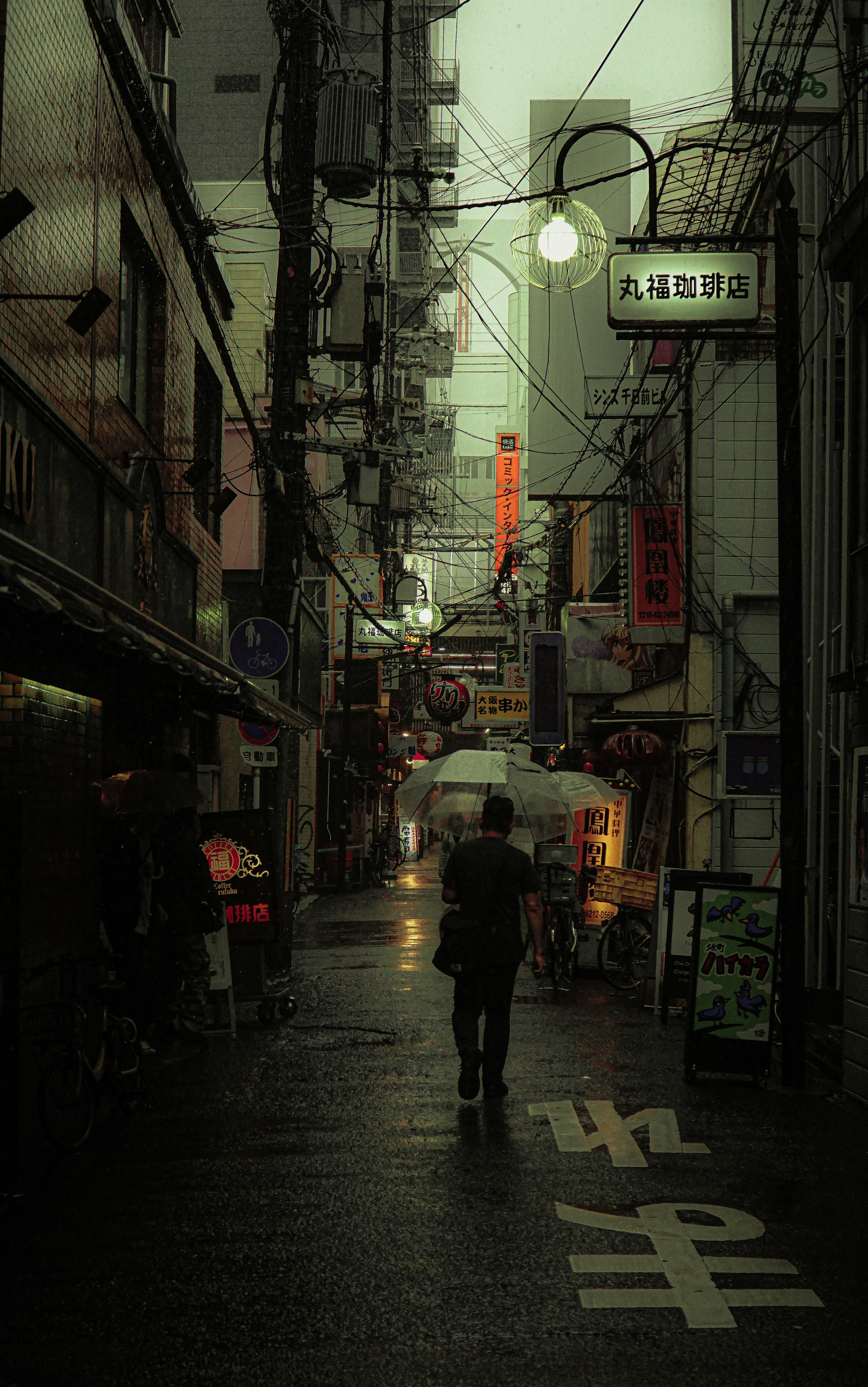 Persona caminando en un callejón oscuro con farolas y lluvia