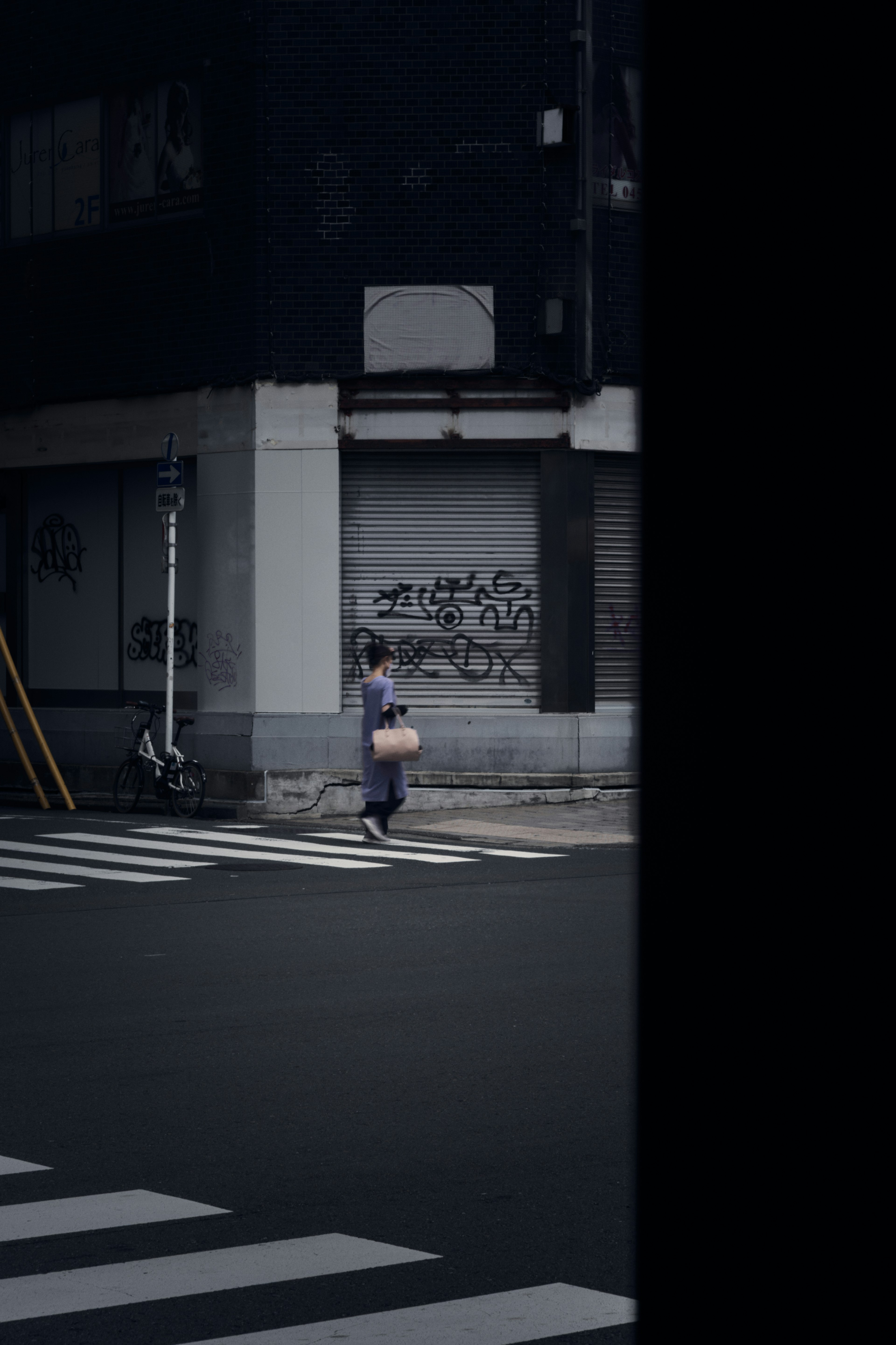 Mujer cruzando una calle oscura con grafitis en un edificio