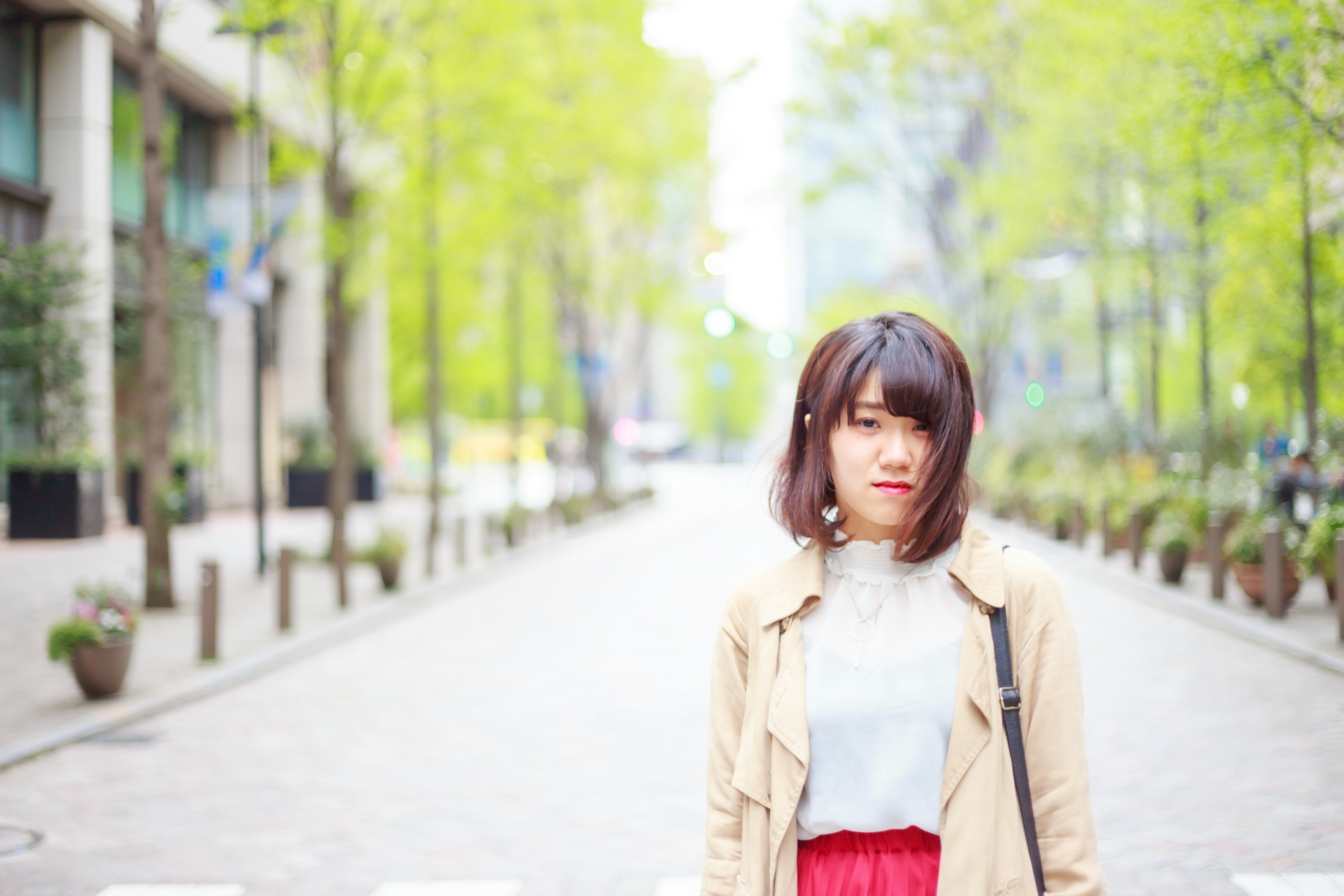 春の街並みで立つ女性　緑の木々とぼかし背景