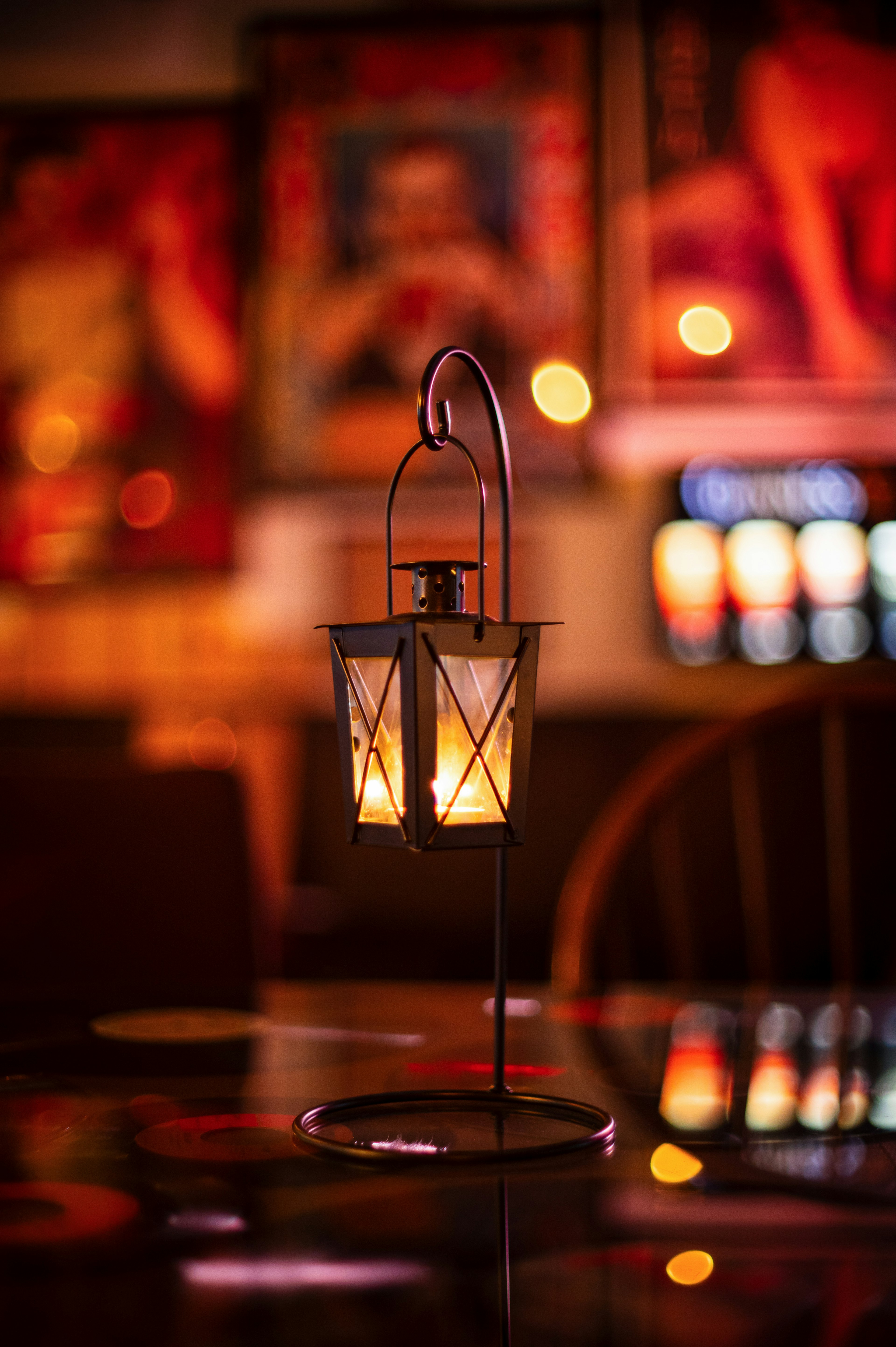 A lantern placed on a table emitting warm light with colorful art in the background