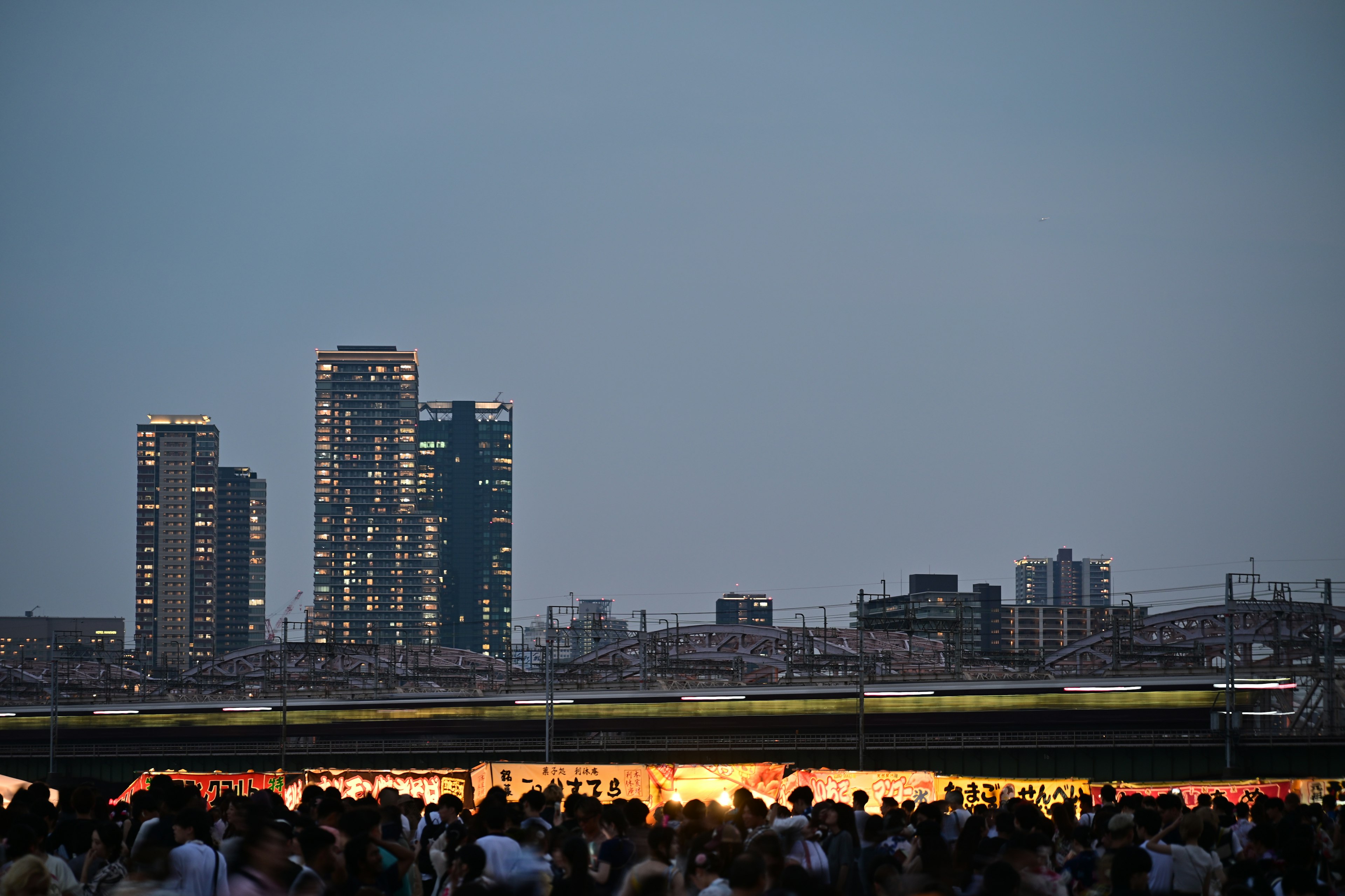 Crowd gathered at dusk with illuminated skyscrapers in the background